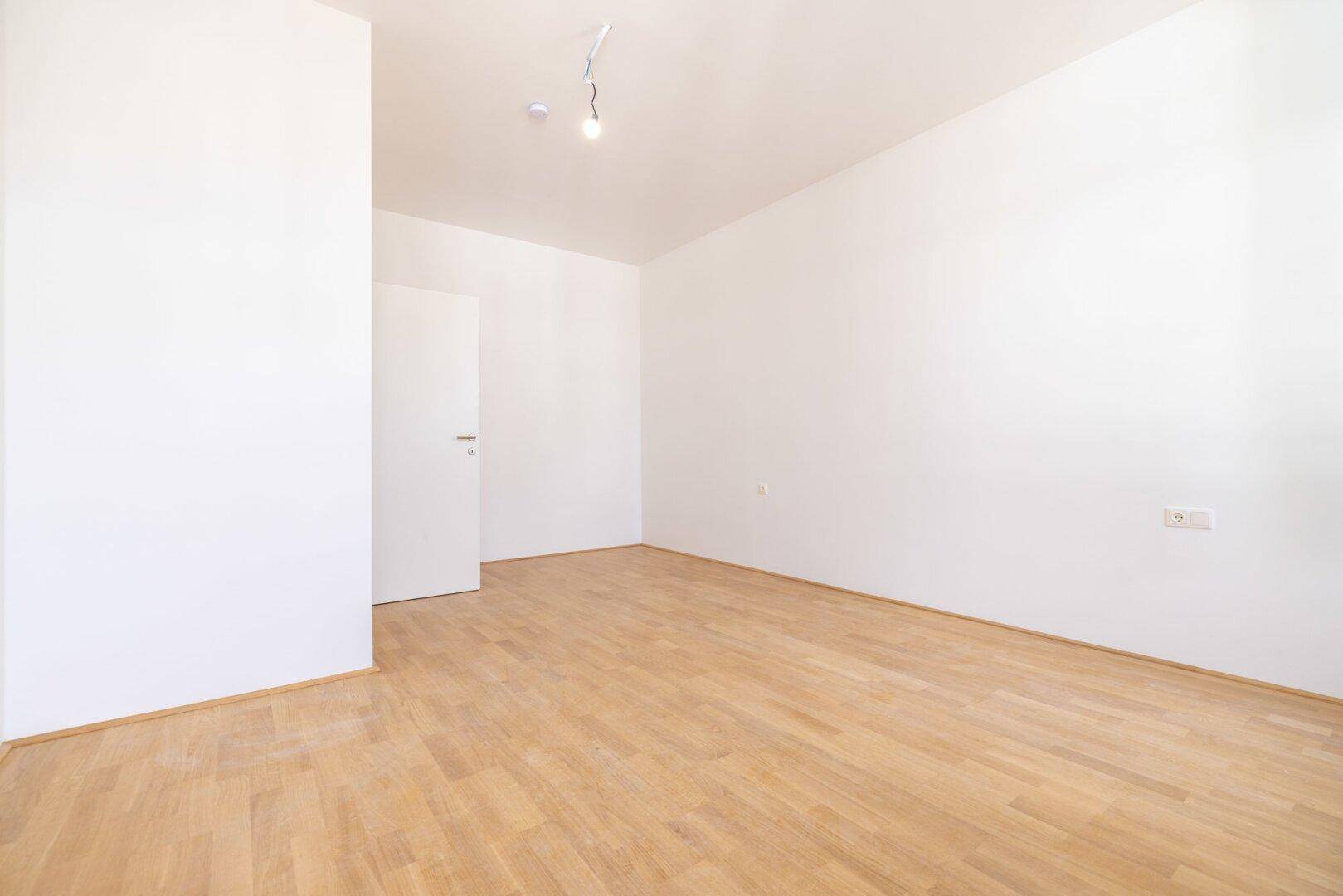 Leeres Zimmer mit weiß gestrichenen Wänden und hellem Parkettboden, bietet vielseitige Nutzungsmöglichkeiten.