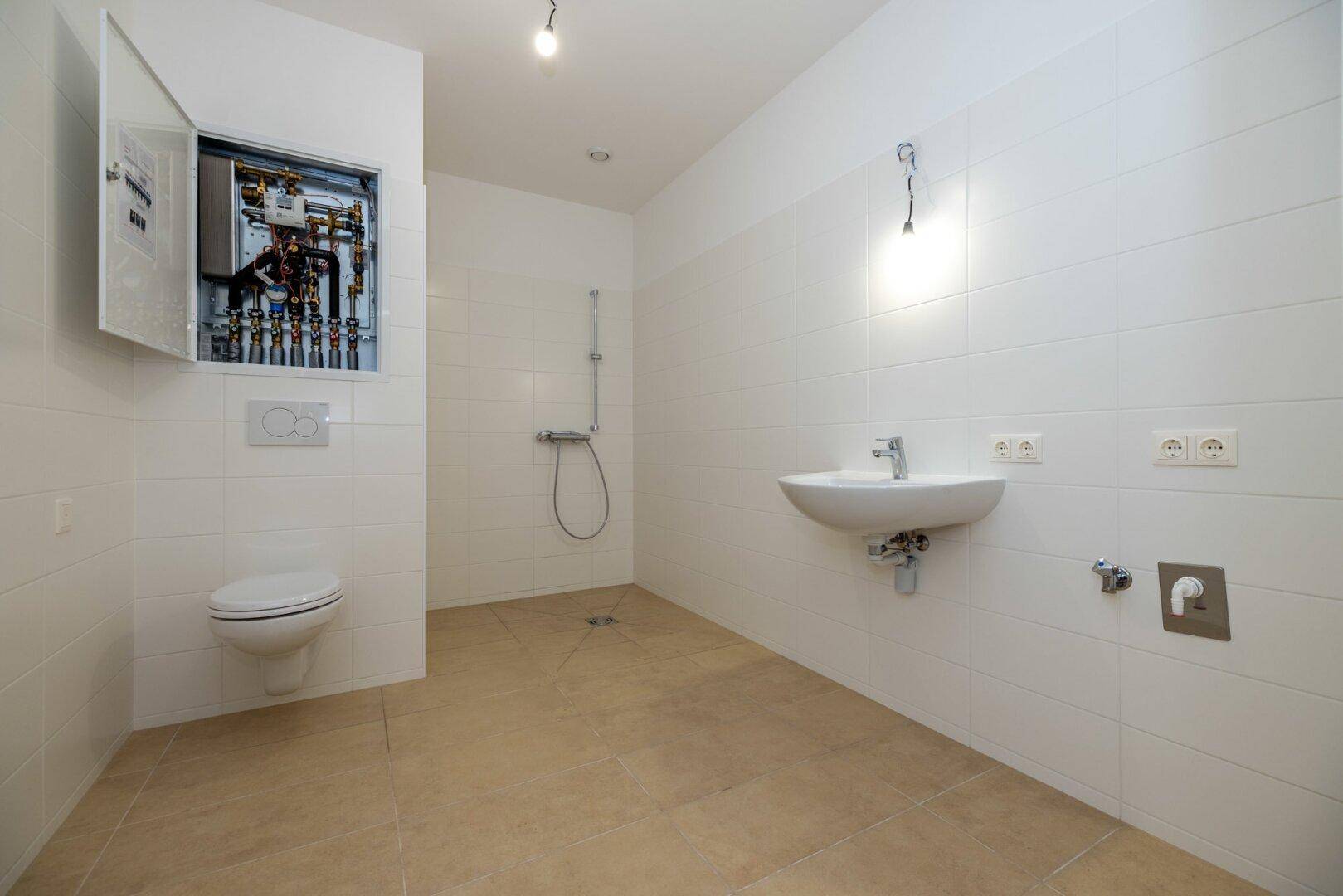 Modernes Badezimmer mit WC, Waschbecken und Duschbereich, hell gefliest und funktional ausgestattet.