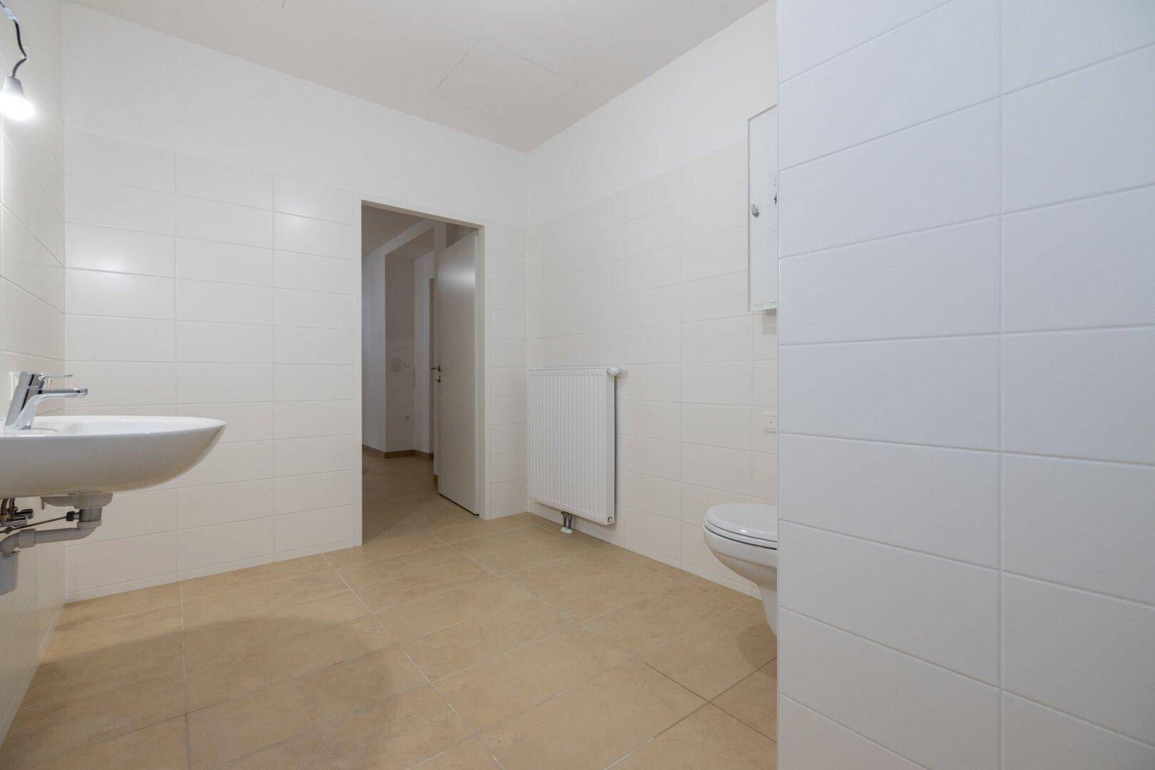 Funktionales Badezimmer mit Waschbecken, WC und Zugang zu einem weiteren Raum, praktisch und hell.