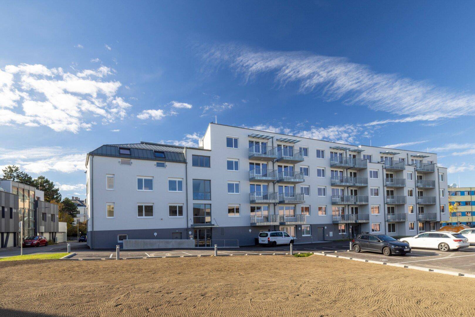 Neubau-Wohngebäude mit Balkonen und Parkplätzen im Freien, in einer sonnigen Umgebung gelegen.
