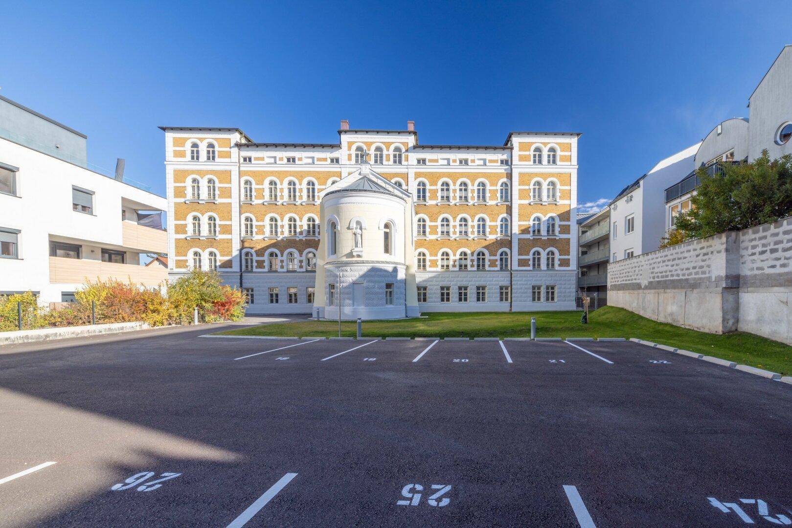 Historisches Gebäude mit aufwendiger Fassade und einem Vorplatz mit Parkplätzen, beeindruckende Architektur.