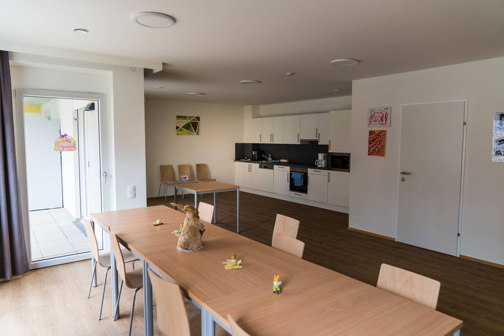 Heller Gemeinschaftsraum mit langer Tafel und integrierter Küchenzeile, ideal für gemeinsame Mahlzeiten.