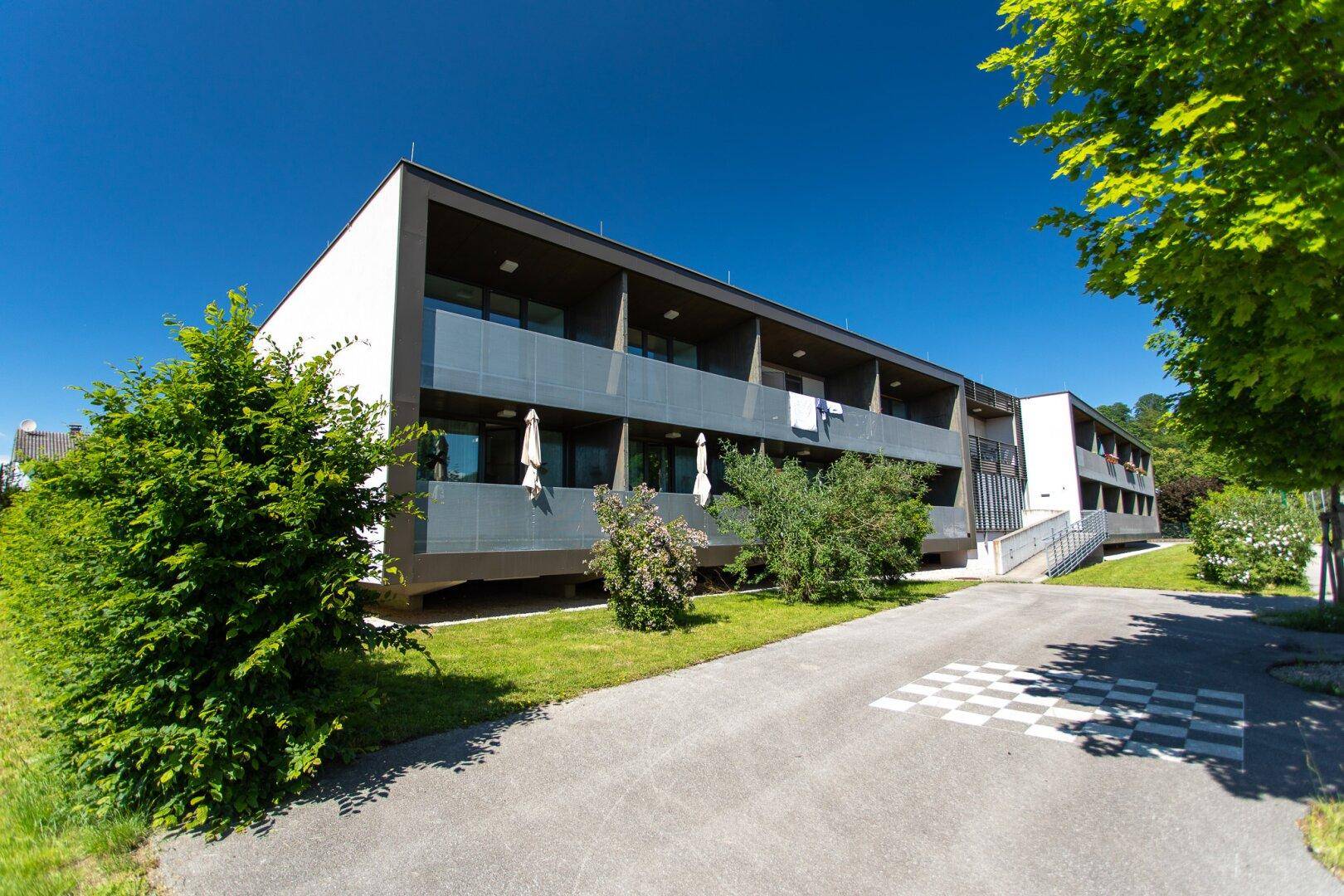 Modernes Wohngebäude mit Balkonen und gepflegter Grünanlage unter blauem Himmel.