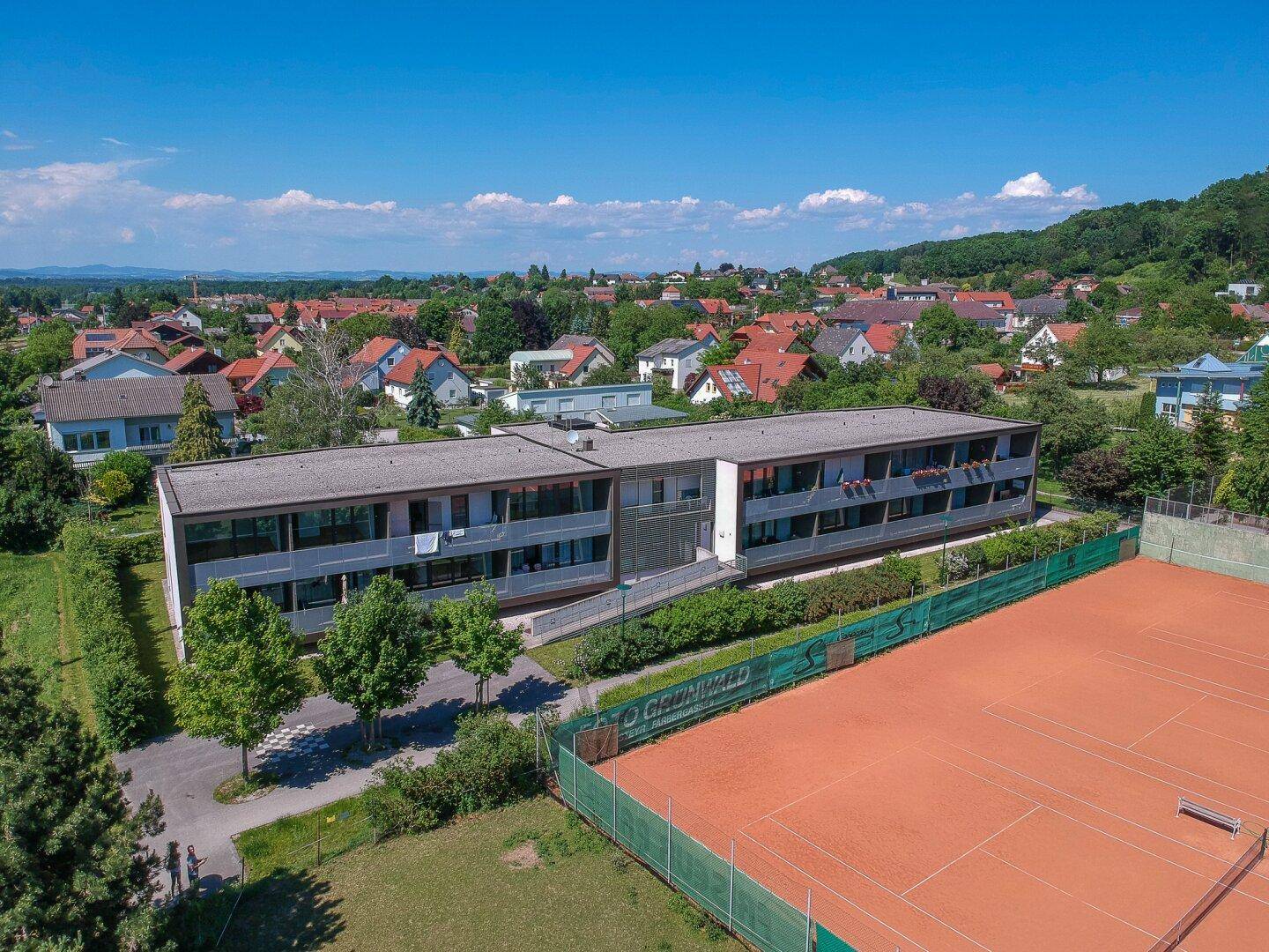 Weitläufige Luftaufnahme der Wohnanlage mit Tennisplatz und ländlicher Umgebung.