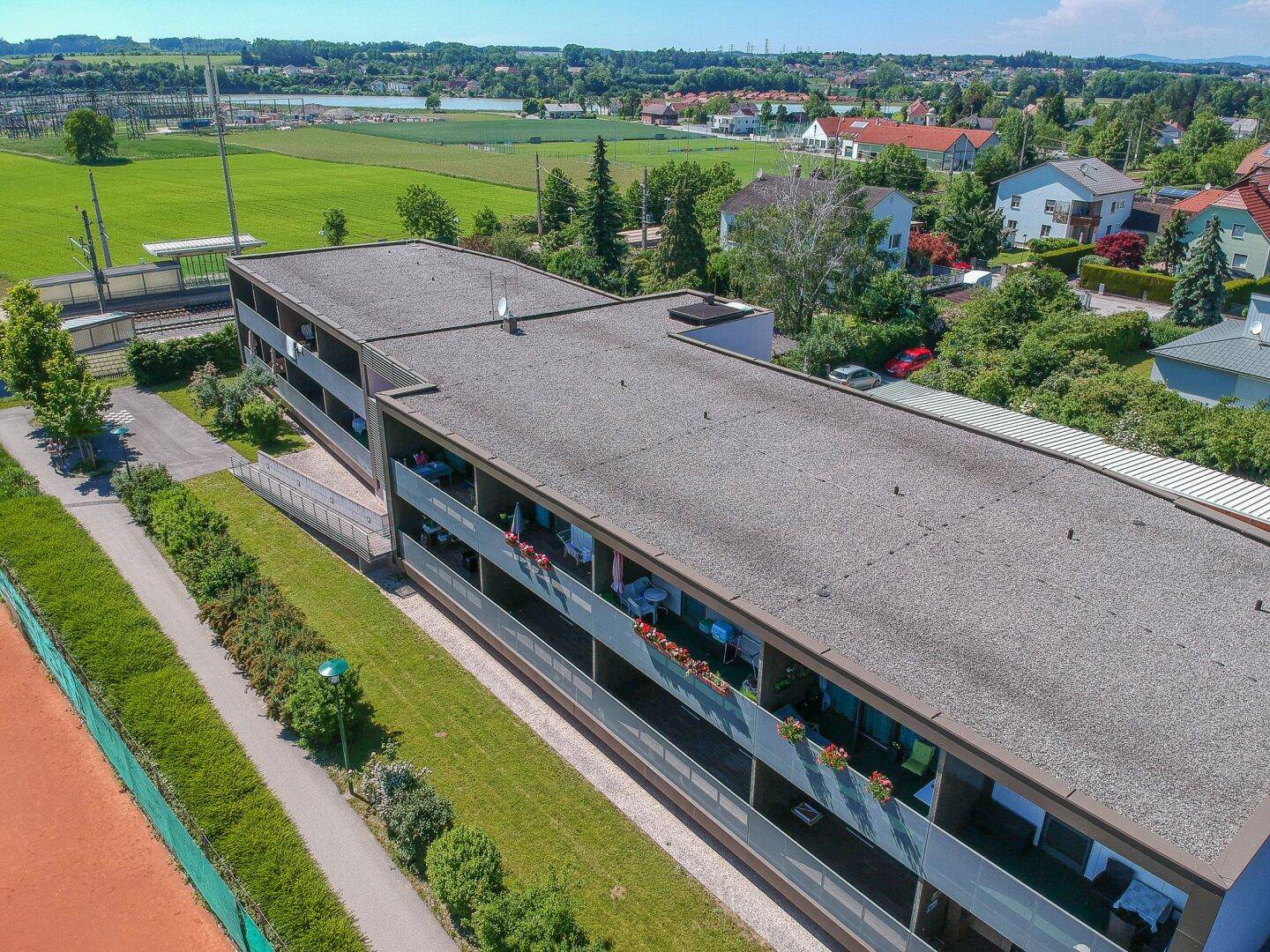 Dachansicht der Wohnanlage mit Flachdach und angrenzendem Tennisplatz.