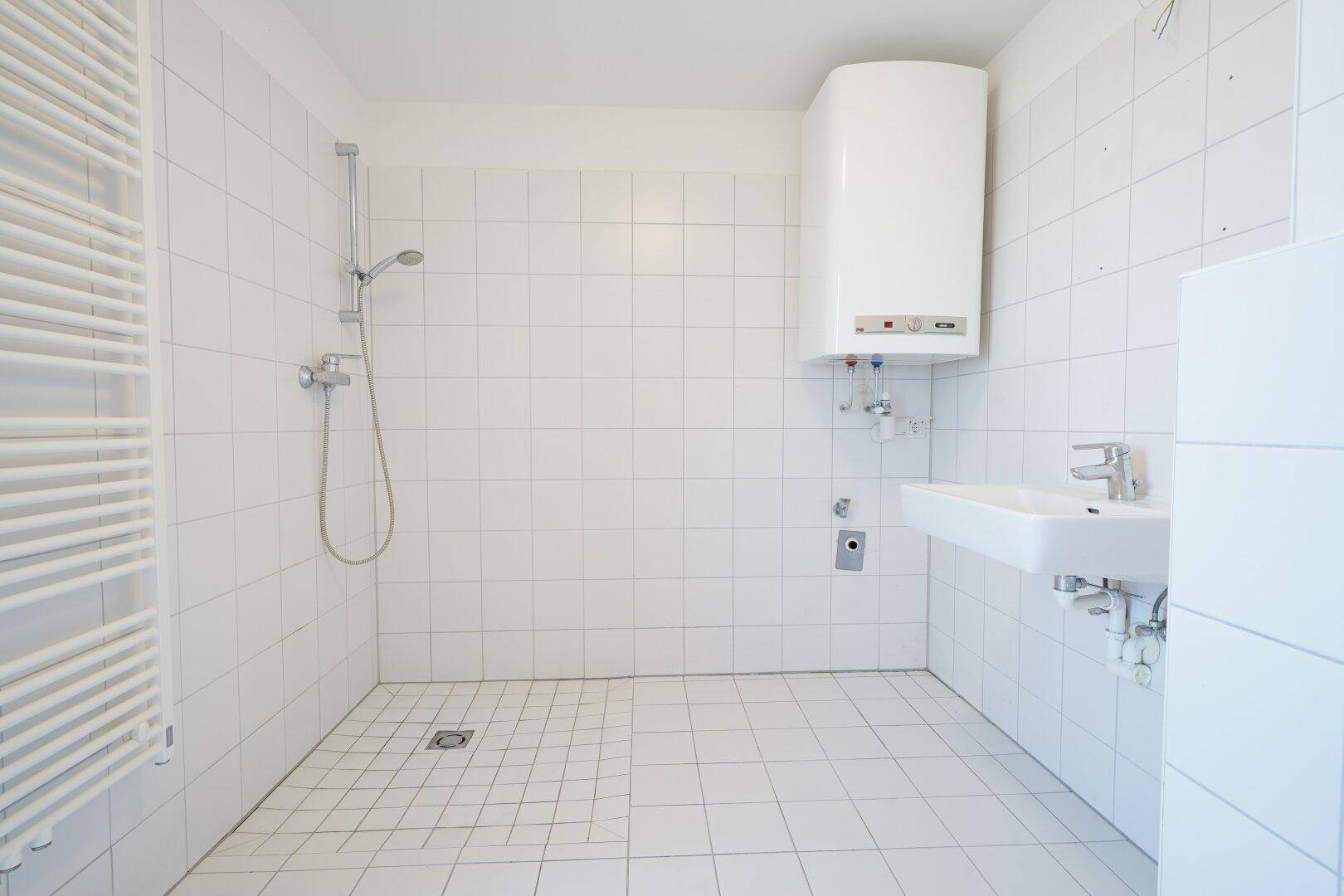 Modern gefliestes Badezimmer mit Dusche, Waschbecken und Warmwasserboiler.