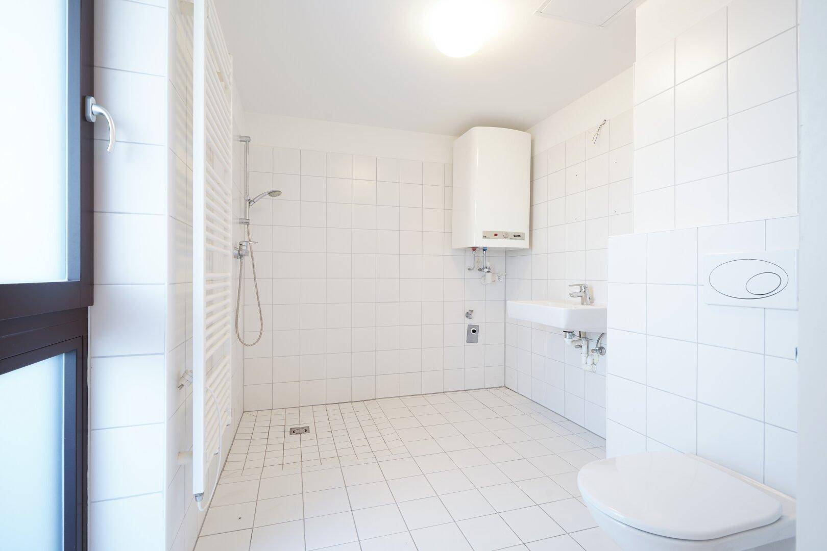 Helles Badezimmer mit weißen Fliesen, Dusche, WC und Fenster für Tageslicht.