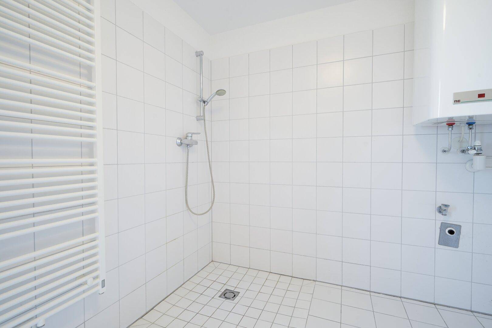Gefliestes Badezimmer mit Duschbereich und Heizkörper, der als Handtuchhalter dient.