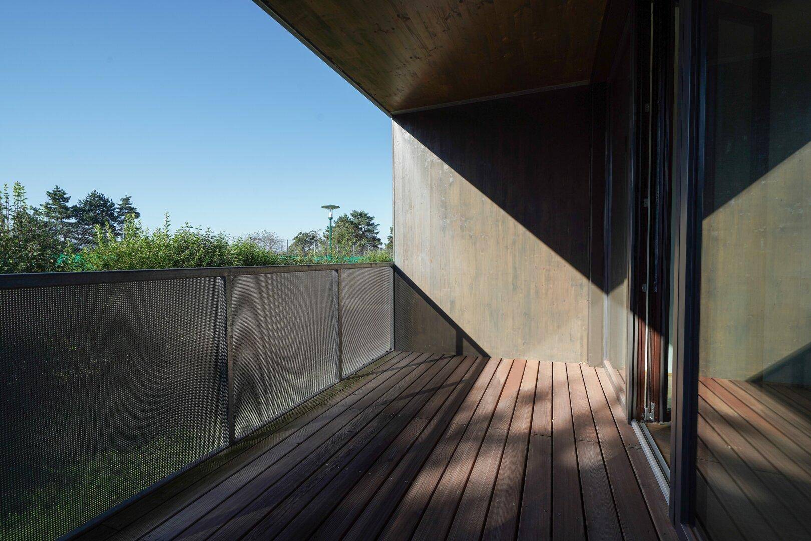Geräumiger Balkon mit Holzboden und moderner Metallbrüstung unter blauem Himmel.