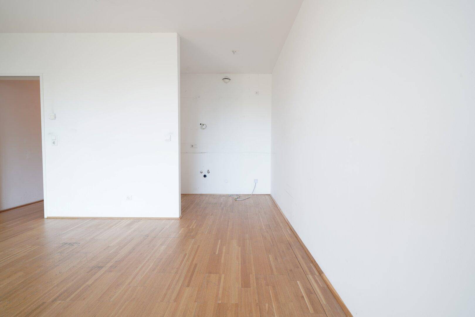 Heller, leerer Raum mit Holzboden und vorbereiteten Anschlüssen an der Wand.