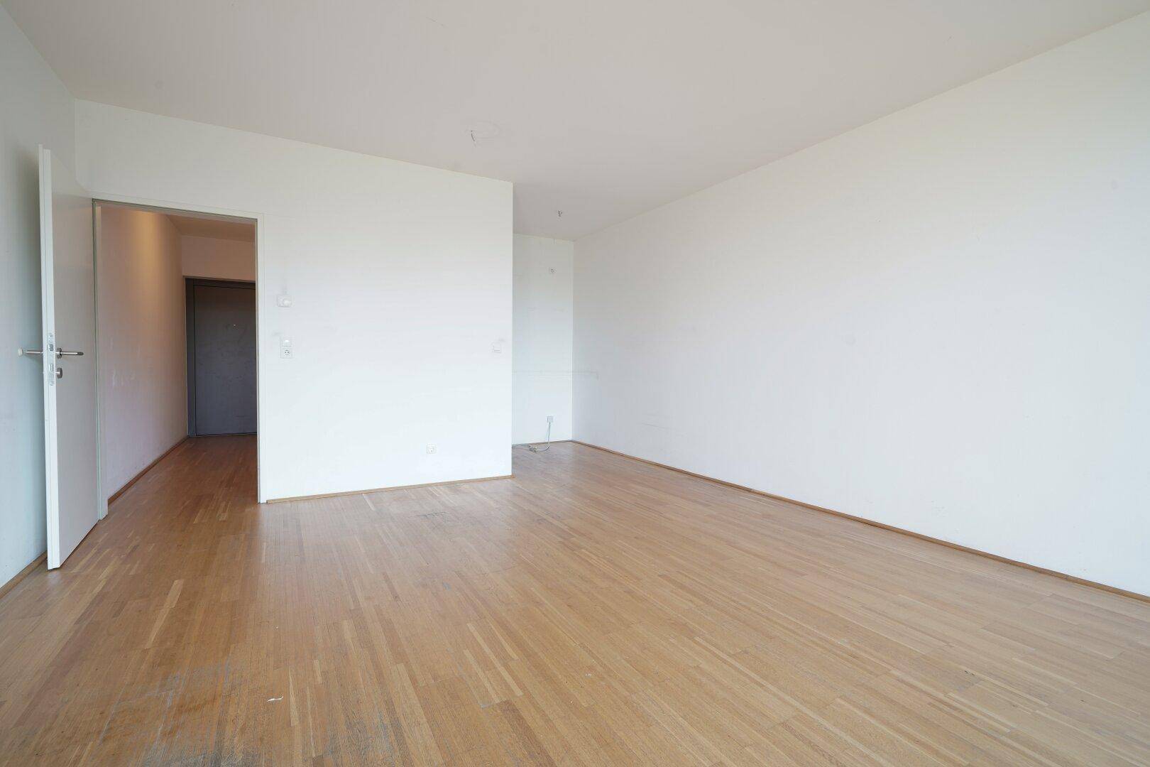 Geräumiger, heller Raum mit Holzboden und Zugang zu einem weiteren Bereich.