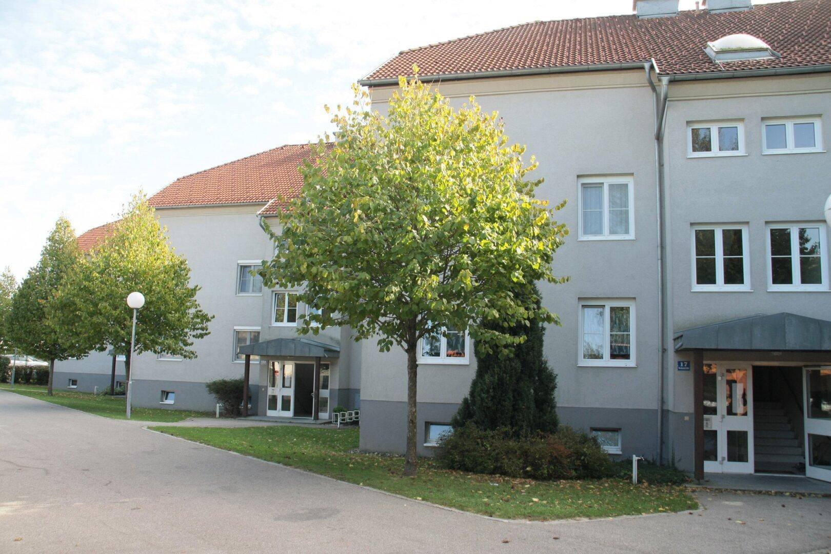 Gepflegtes Mehrfamilienhaus mit heller Fassade, roten Ziegeldächern und grüner Umgebung.