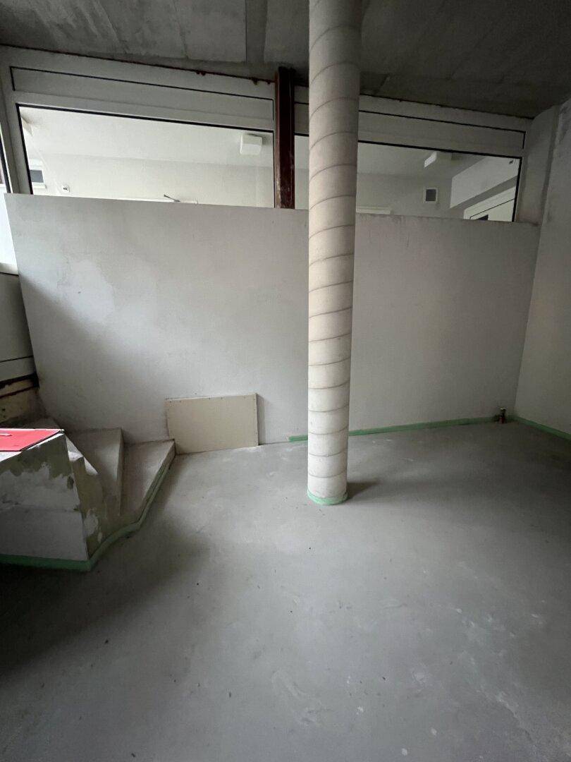 Unfertiger Innenraum mit einer zentralen Säule und großen Fenstern im oberen Bereich.