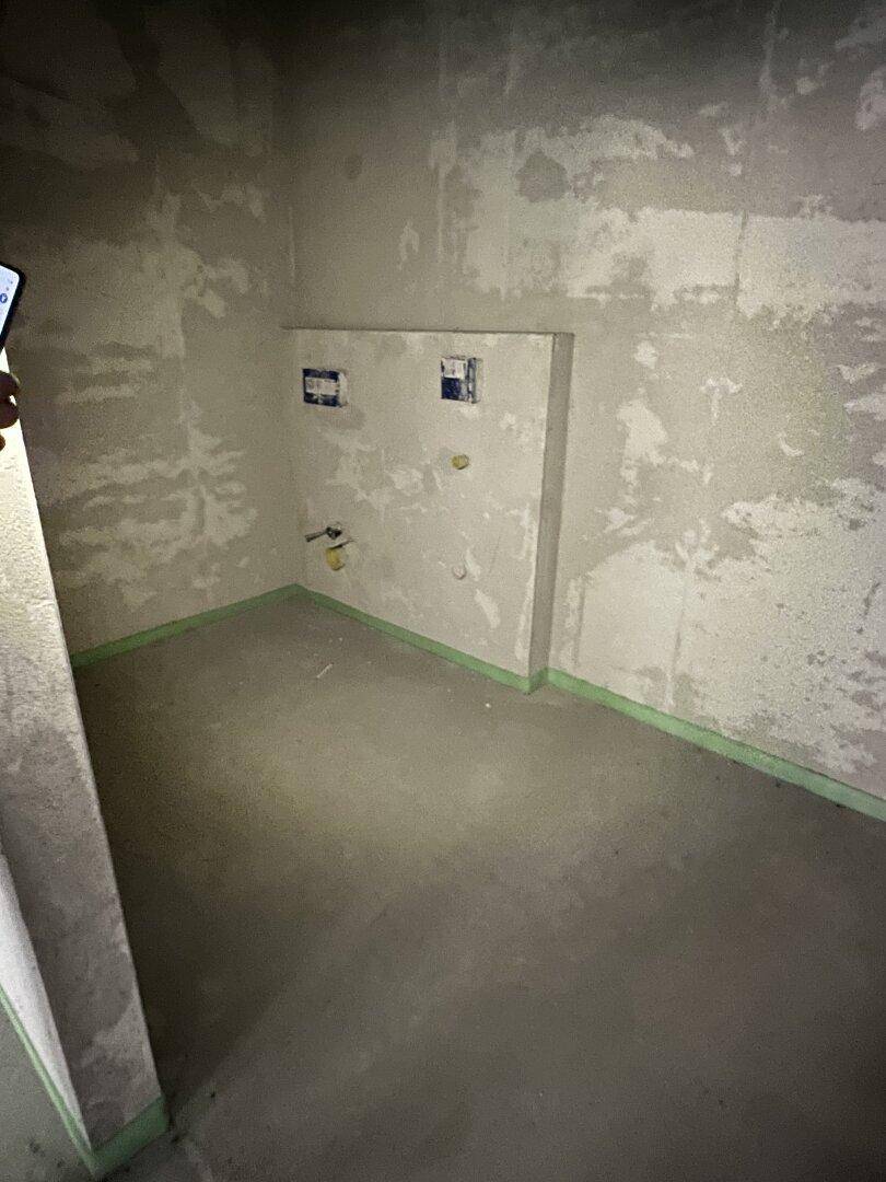 Unfertiger Badezimmerraum mit Wandinstallationen für Toilette oder Waschbecken.