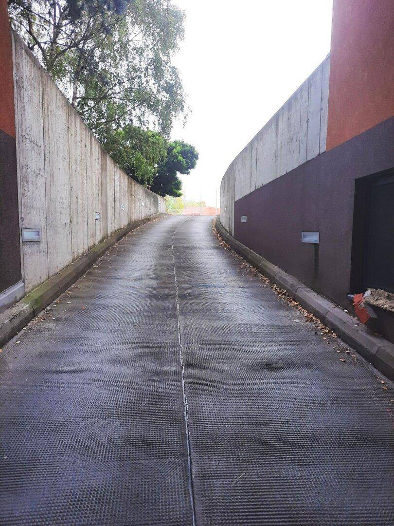 Steile Auffahrt zur Tiefgarage, umgeben von hohen Betonwänden und etwas Vegetation am oberen Ende.