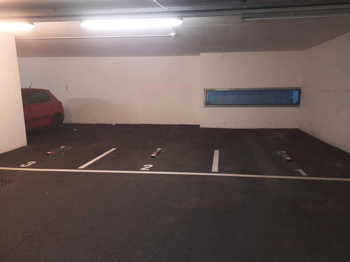 Tiefgaragenstellplätze mit Nummern und einem kleinen Fenster für Belüftung, ein rotes Auto ist geparkt.