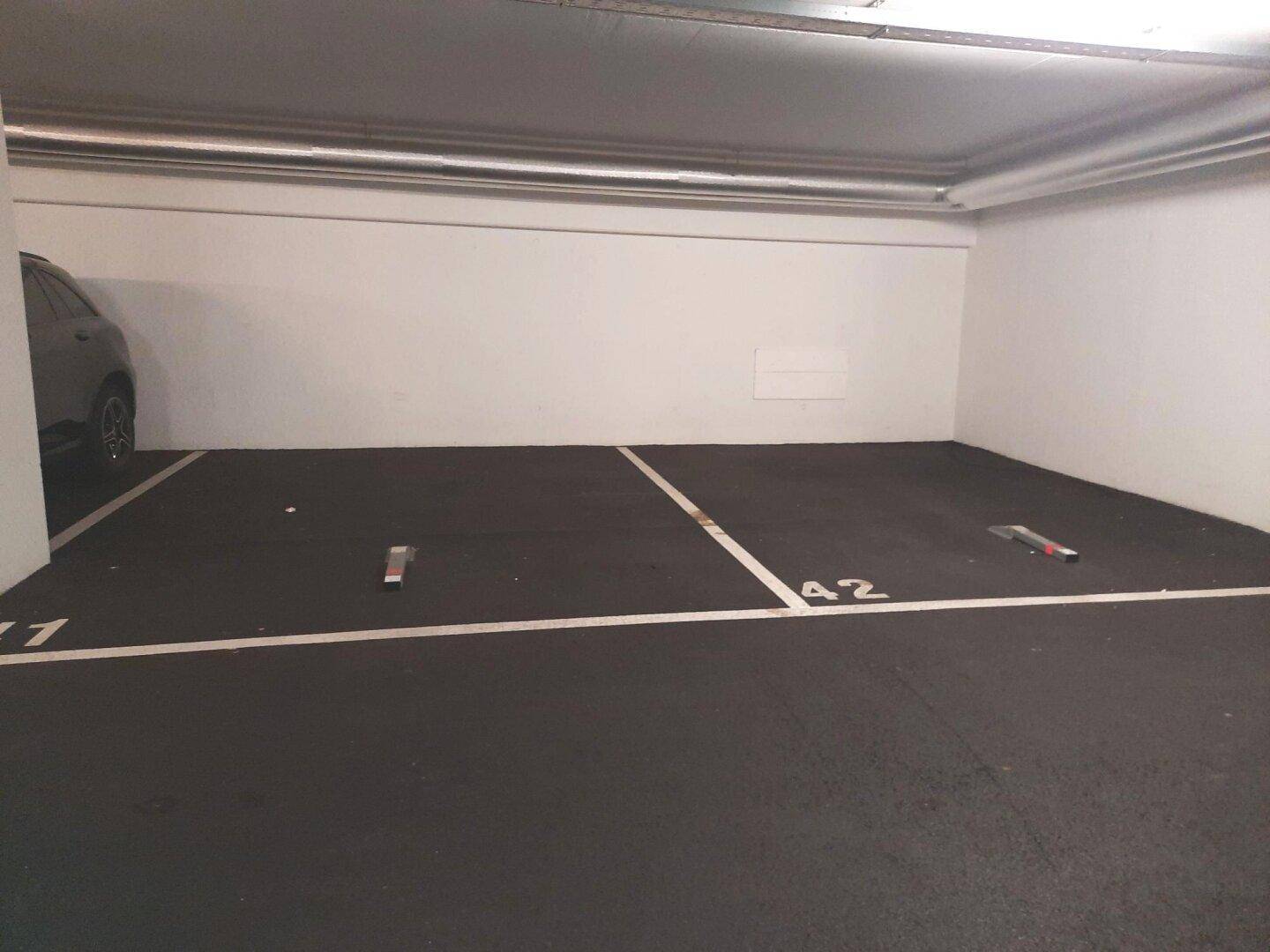 Geräumiger Tiefgaragenstellplatz Nummer 42 mit sichtbaren Deckenrohren und einem geparkten Auto im Hintergrund.