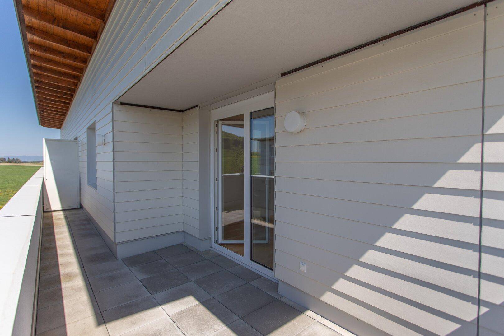 Balkon mit Fliesenboden und Holzverkleidung an der Fassade, bietet viel Sonnenlicht.