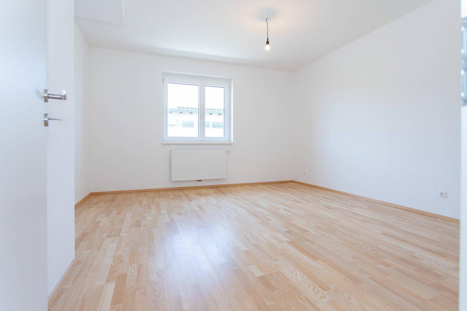 Helles, leeres Zimmer mit Parkettboden und einem Fenster, ideal als Schlaf- oder Arbeitszimmer.