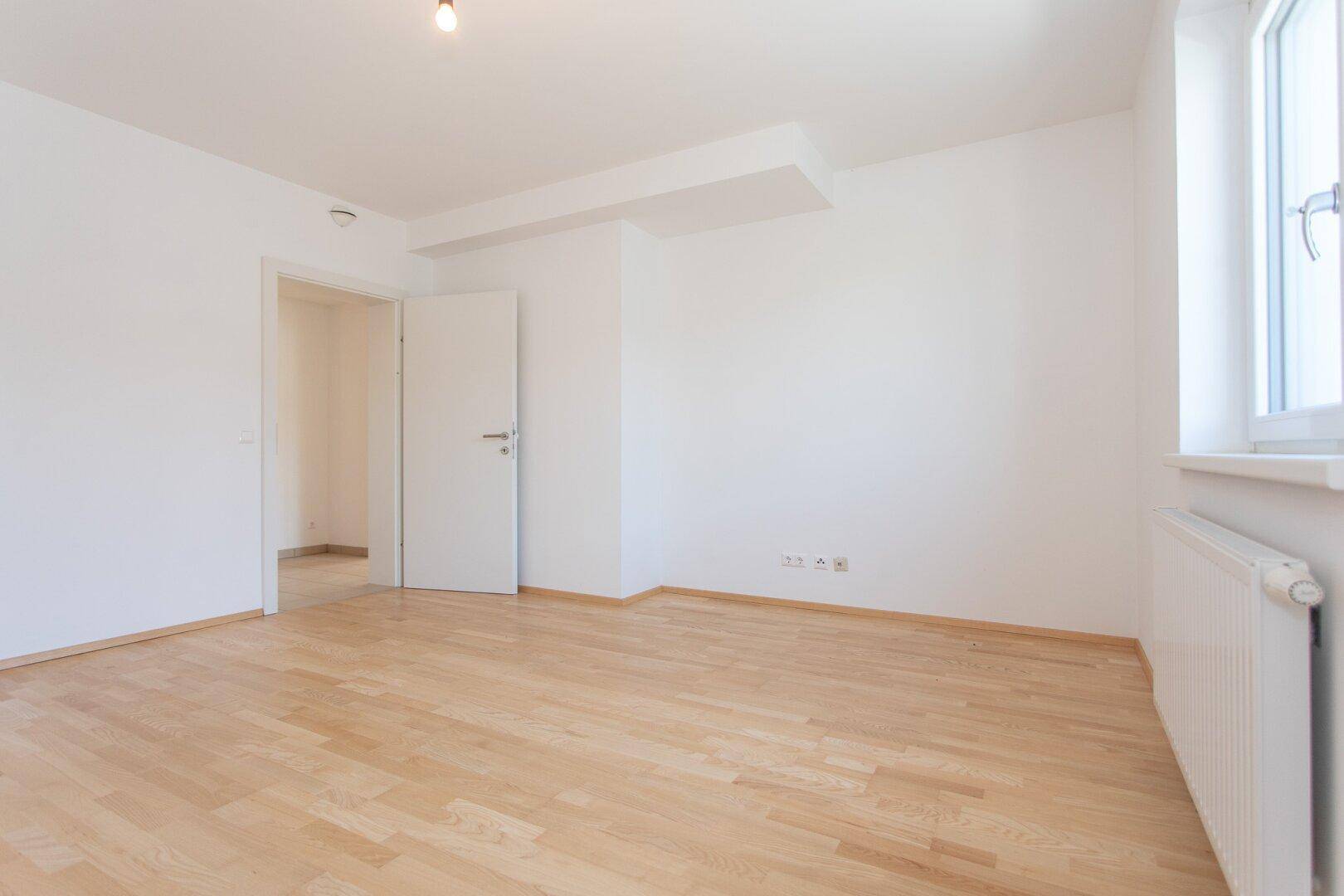 Leeres Zimmer mit Parkettboden und weiß gestrichenen Wänden, bereit für die Einrichtung.