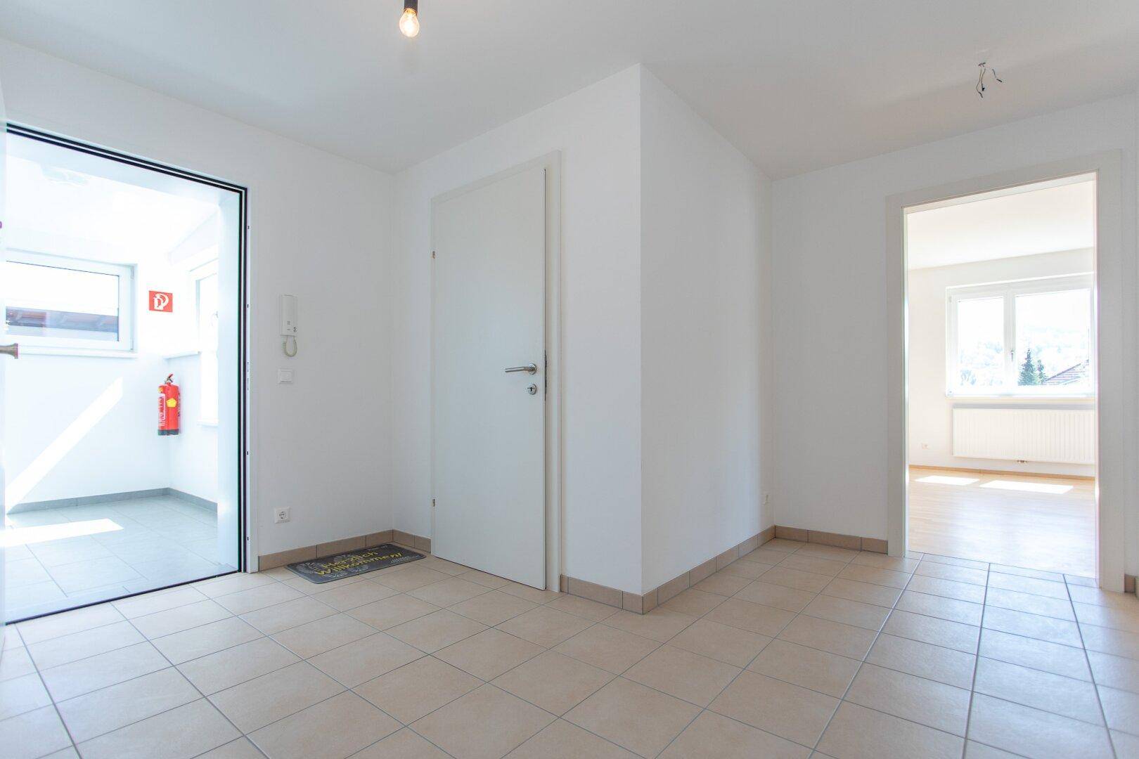 Heller Eingangsbereich mit Fliesenboden und einer Tür, die zu einem weiteren Raum führt.