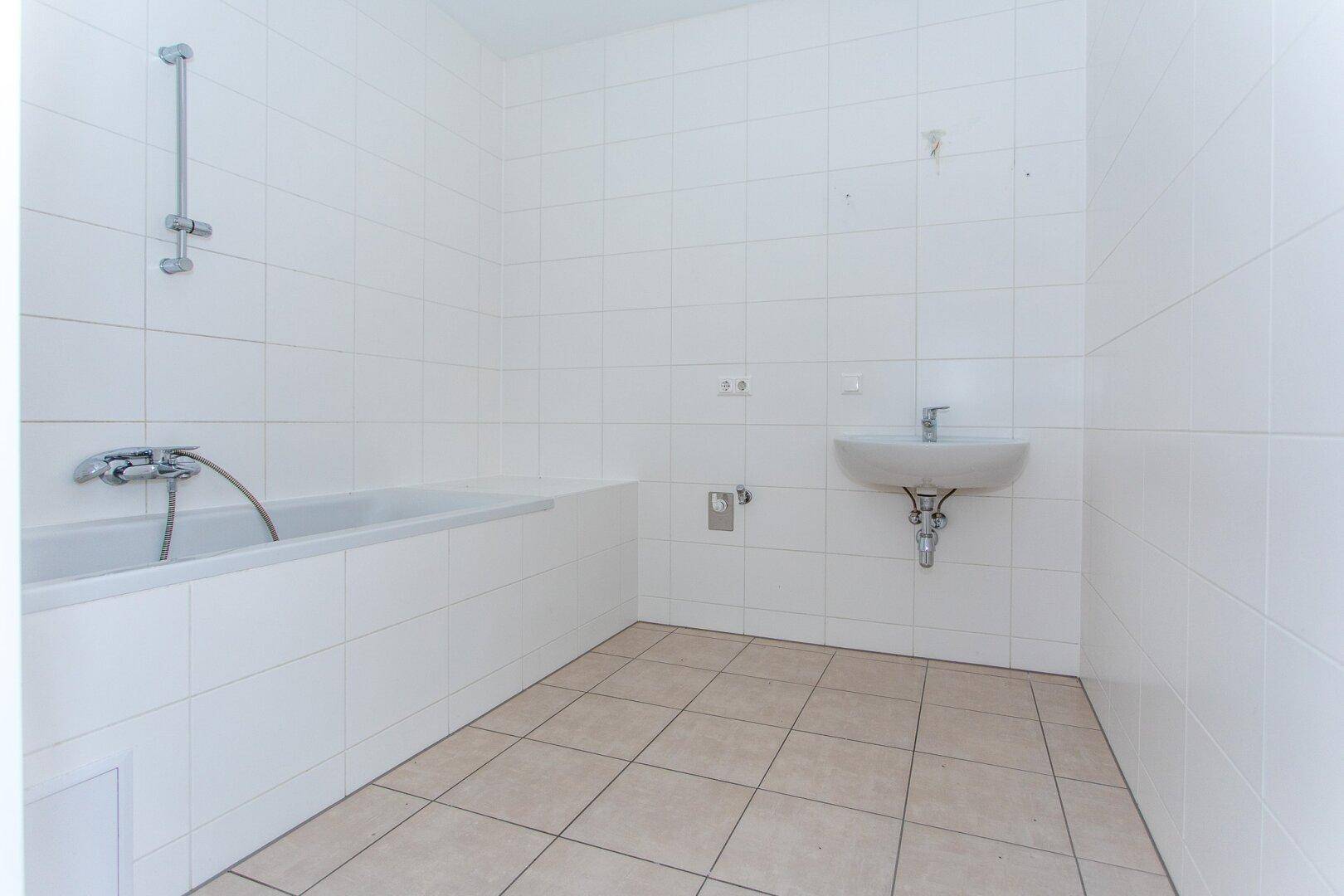 Helles Badezimmer mit weißen Fliesen, Badewanne und Waschbecken, in gutem Zustand.