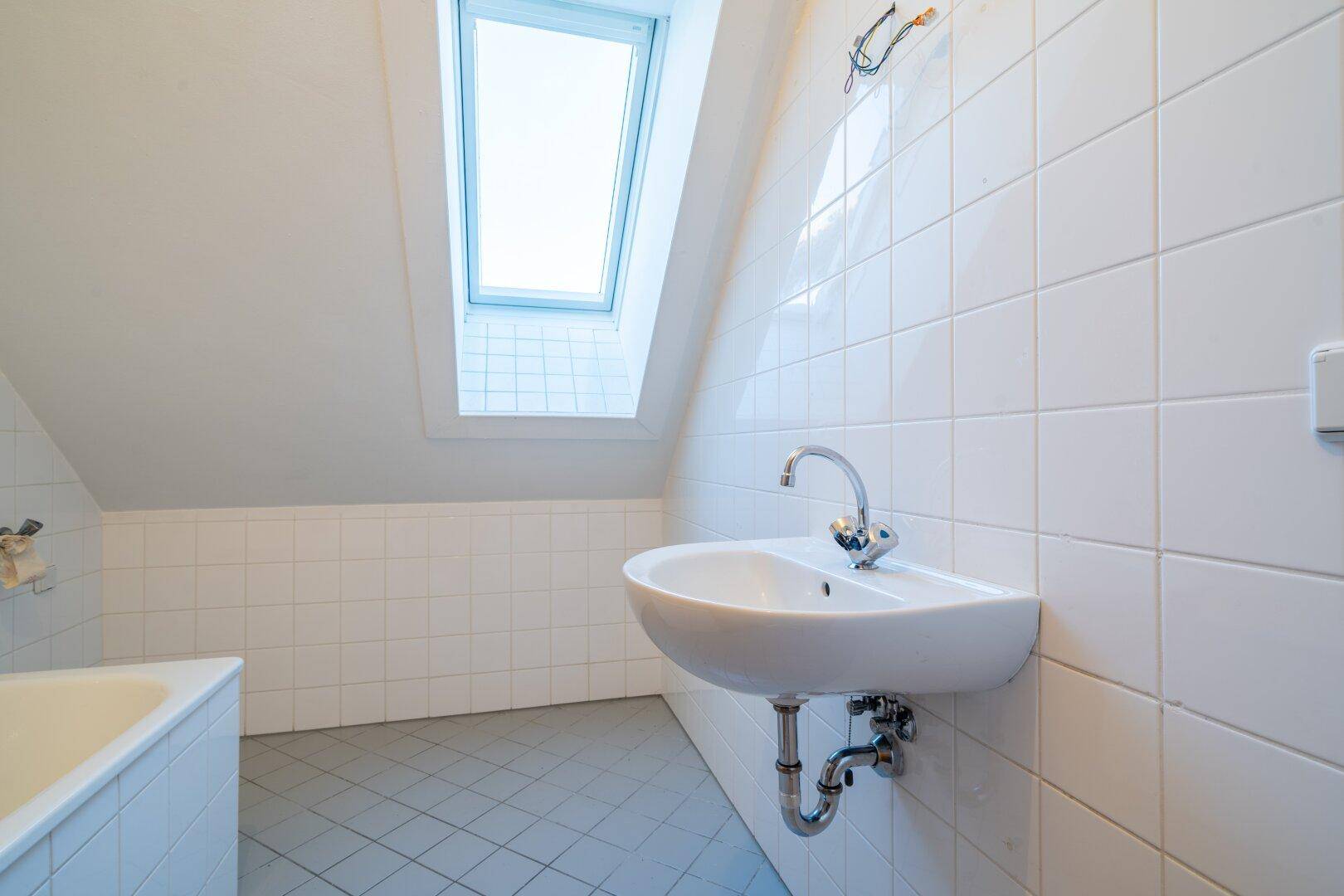 Badezimmer mit weißen Fliesen, einem Waschbecken und einem Dachfenster in der Schräge.