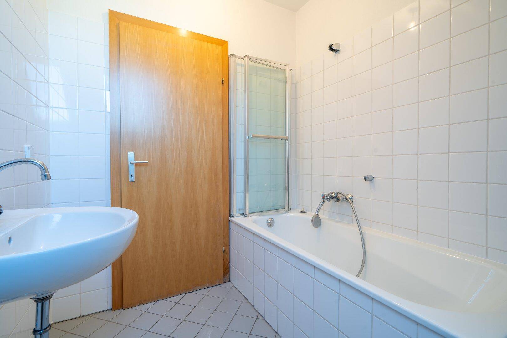 Badezimmer mit weißen Fliesen, einer Badewanne und einem Waschbecken.