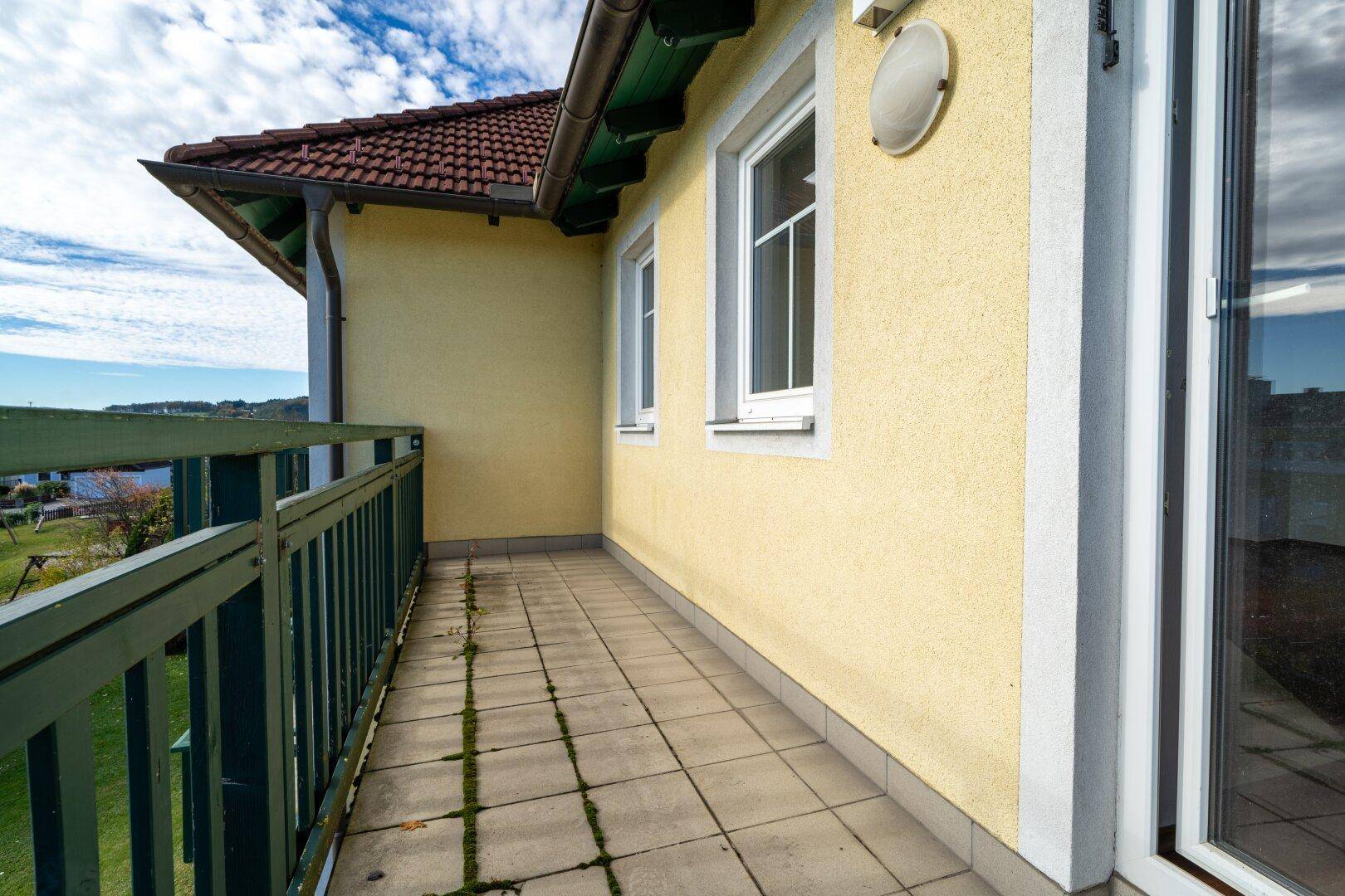 Balkon mit gelber Fassade, Fliesenboden und grünem Geländer, mit Blick auf die Umgebung.