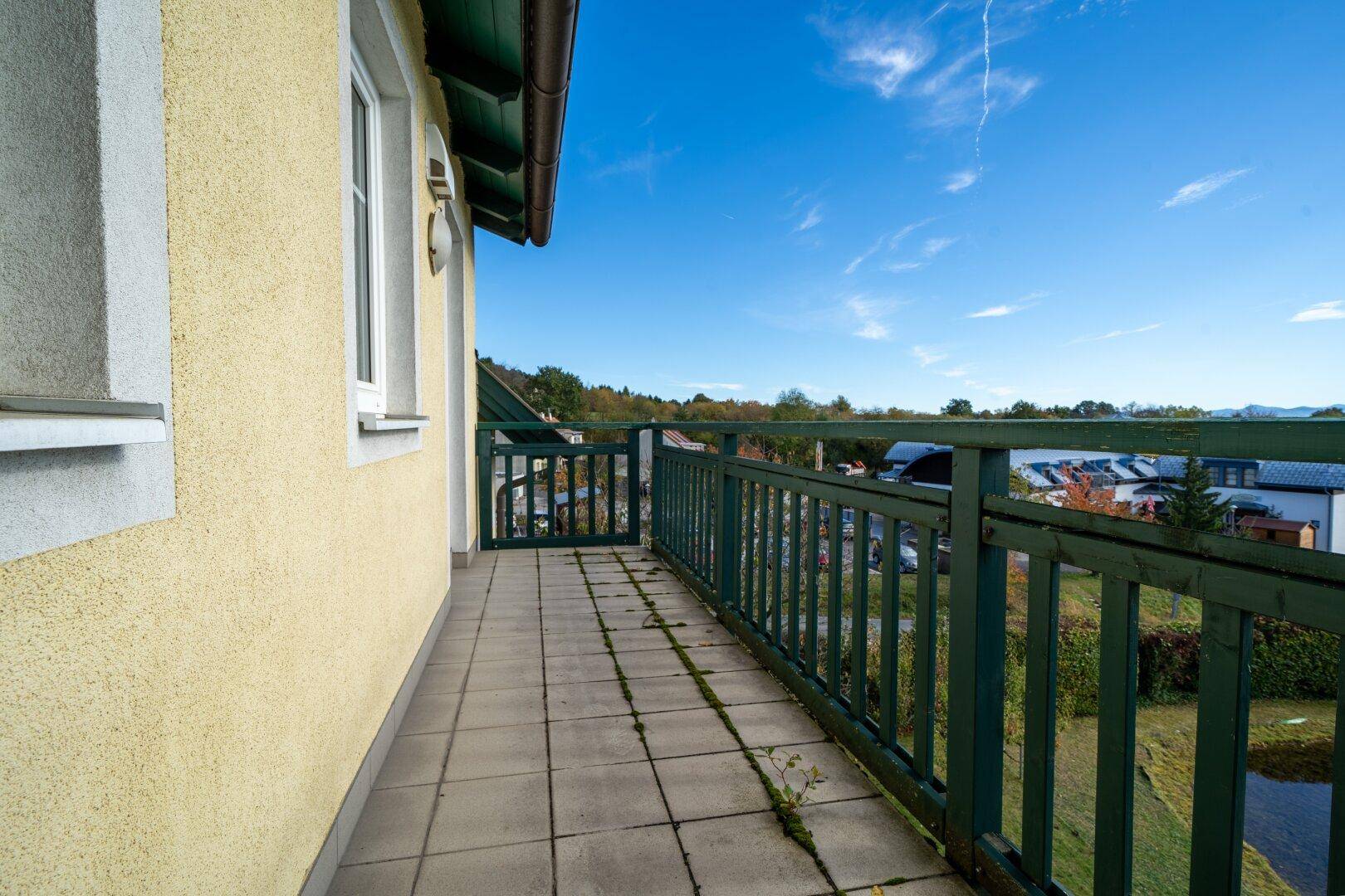 Balkon mit Fliesenboden und grünem Holzgeländer, der einen weiten Blick in die Landschaft bietet.