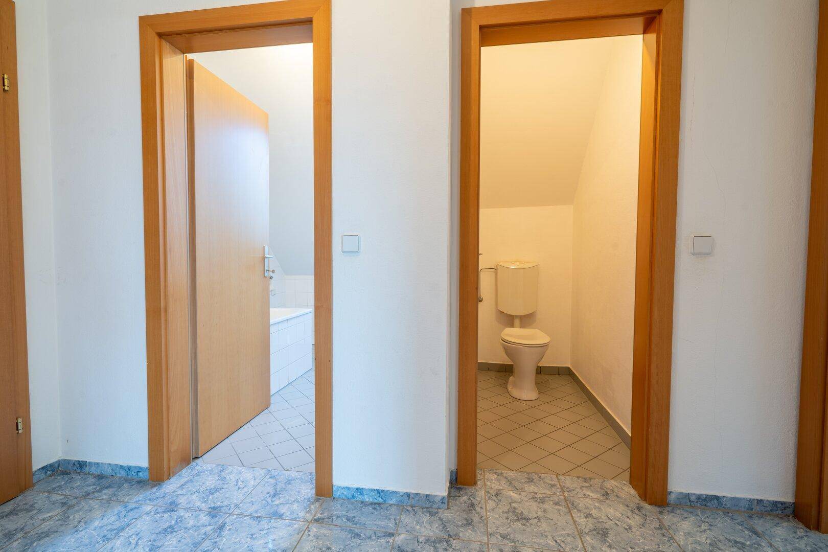 Flur mit Fliesenboden und Holztüren, die zu Bad und WC führen.