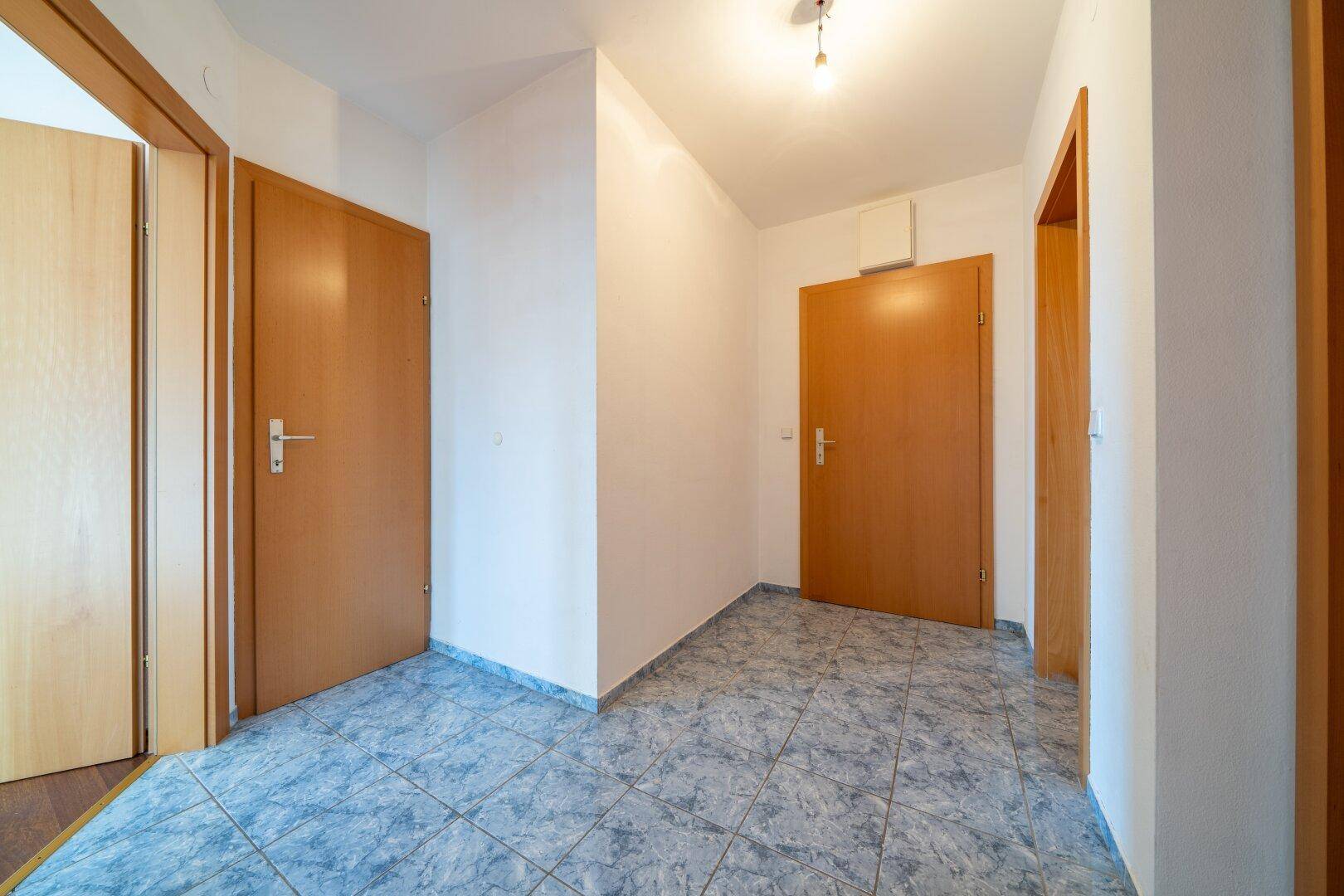 Flur mit gemustertem Fliesenboden und mehreren Holztüren, die den Zugang zu den Zimmern ermöglichen.
