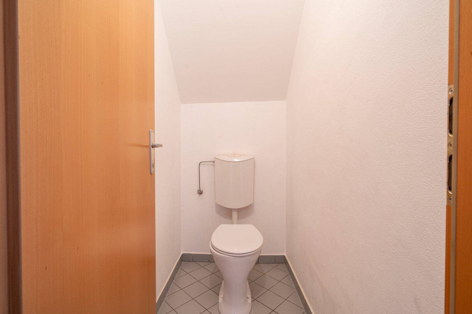 Kleines WC mit Fliesenboden und einer einfachen Toilette.