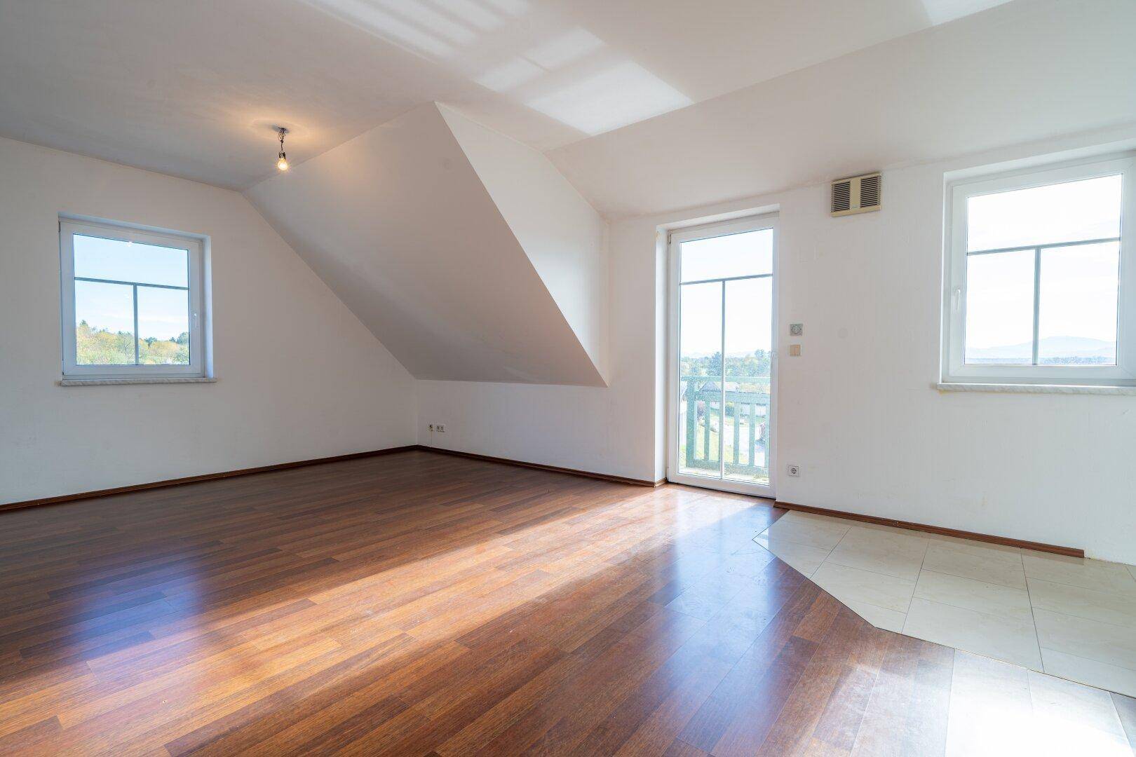 Heller, leerer Raum mit Holzboden, Dachschräge und Zugang zu einem Balkon.
