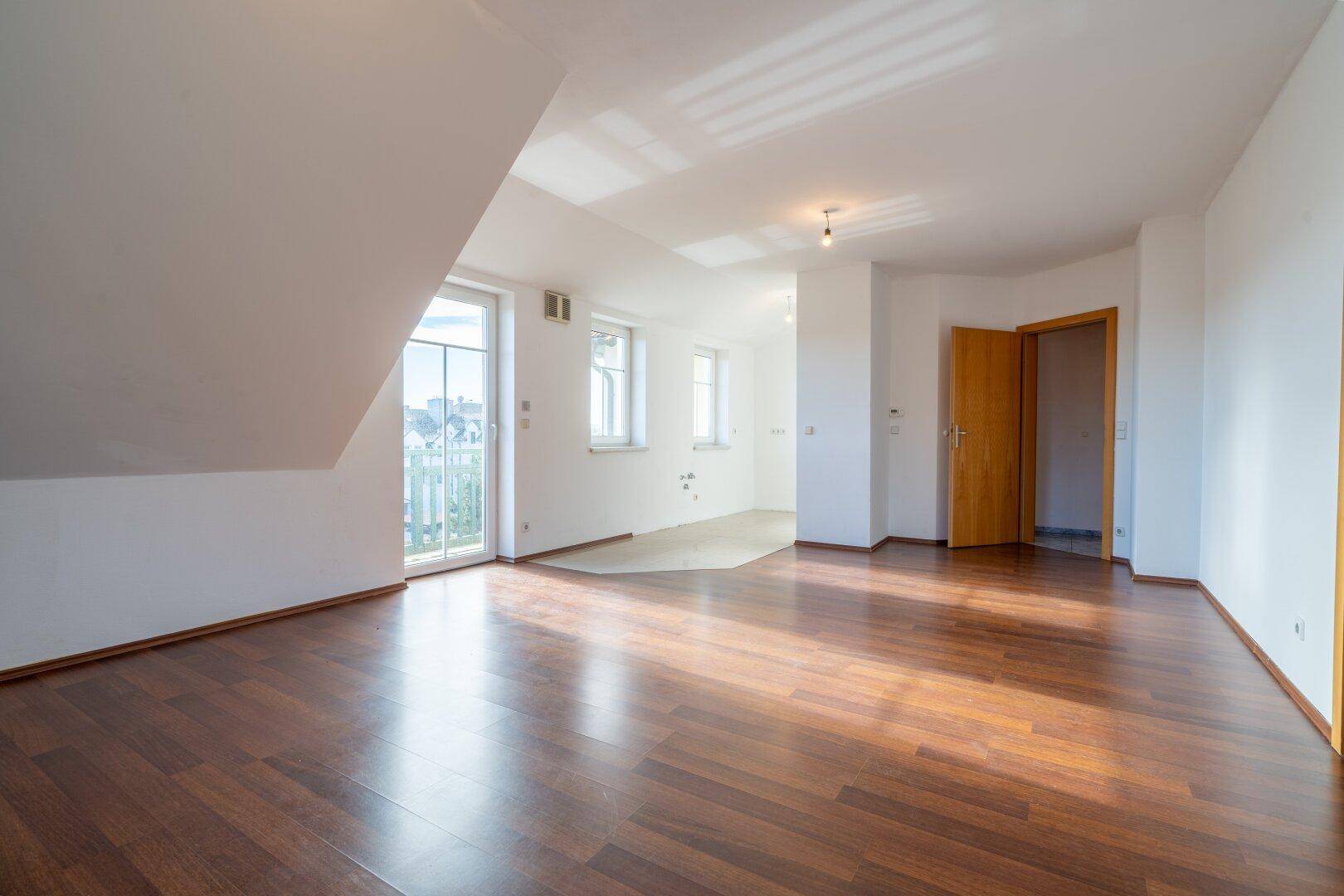 Großer, heller Raum mit Holzboden, Dachschräge und Zugang zu einem Balkon und weiteren Zimmern.
