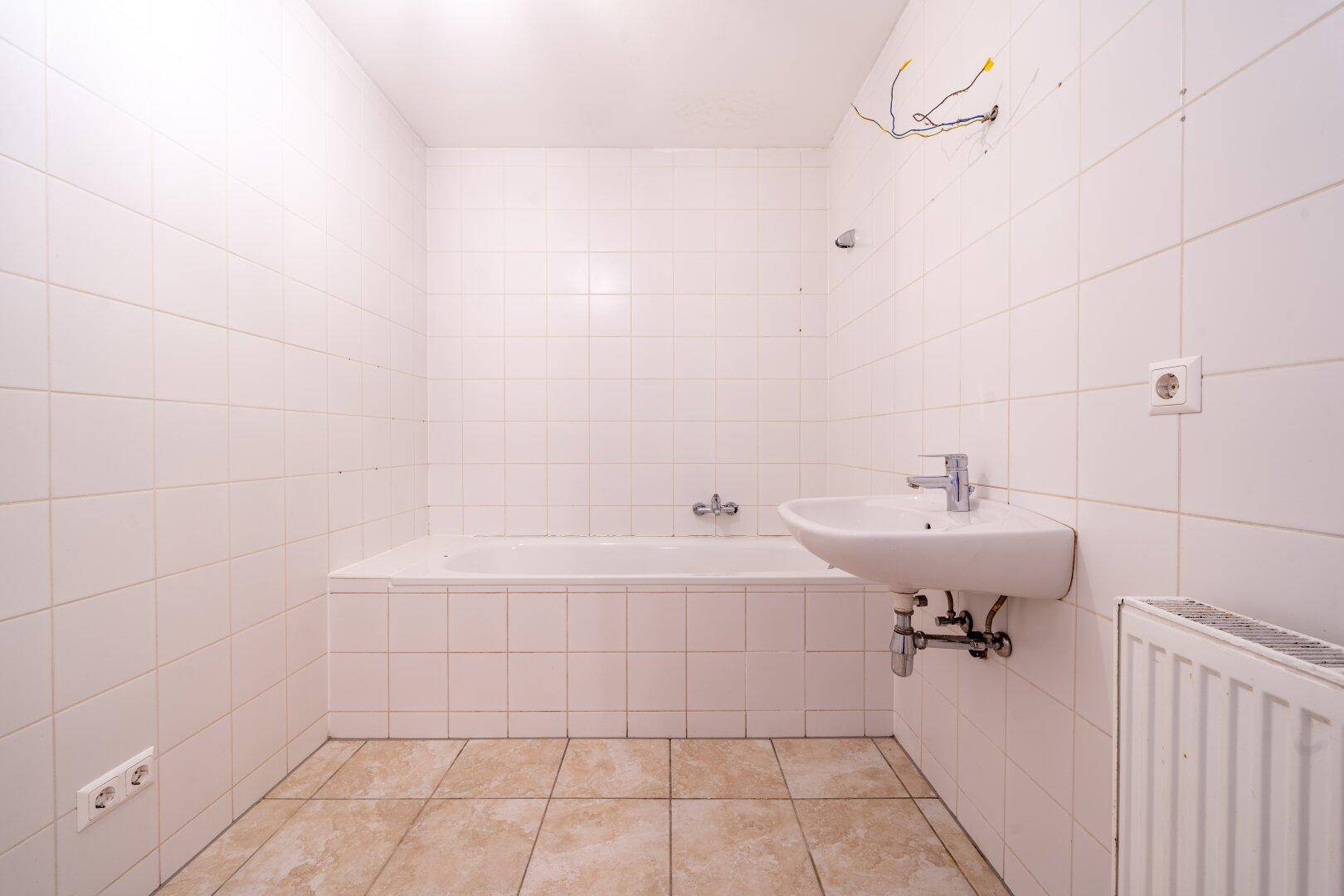 Badezimmer mit Badewanne, Waschbecken und weißen Fliesen, bereit für eine Modernisierung.