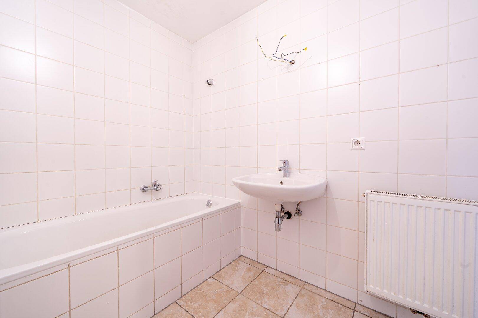 Helles Badezimmer mit Badewanne und Waschbecken, ausgestattet mit klassischen weißen Wandfliesen.