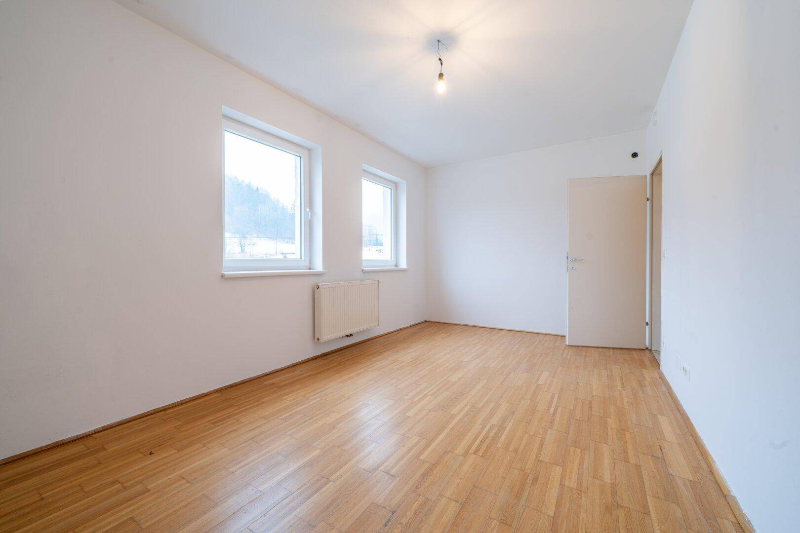 Geräumiges Zimmer mit Parkettboden und zwei Fenstern, bietet vielseitige Nutzungsmöglichkeiten.