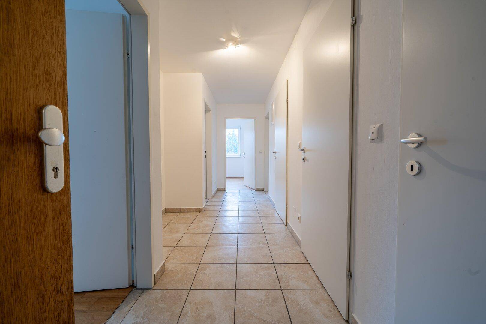 Langer Flur mit beigefarbenen Fliesen, der zu weiteren Zimmern mit Parkettboden führt.