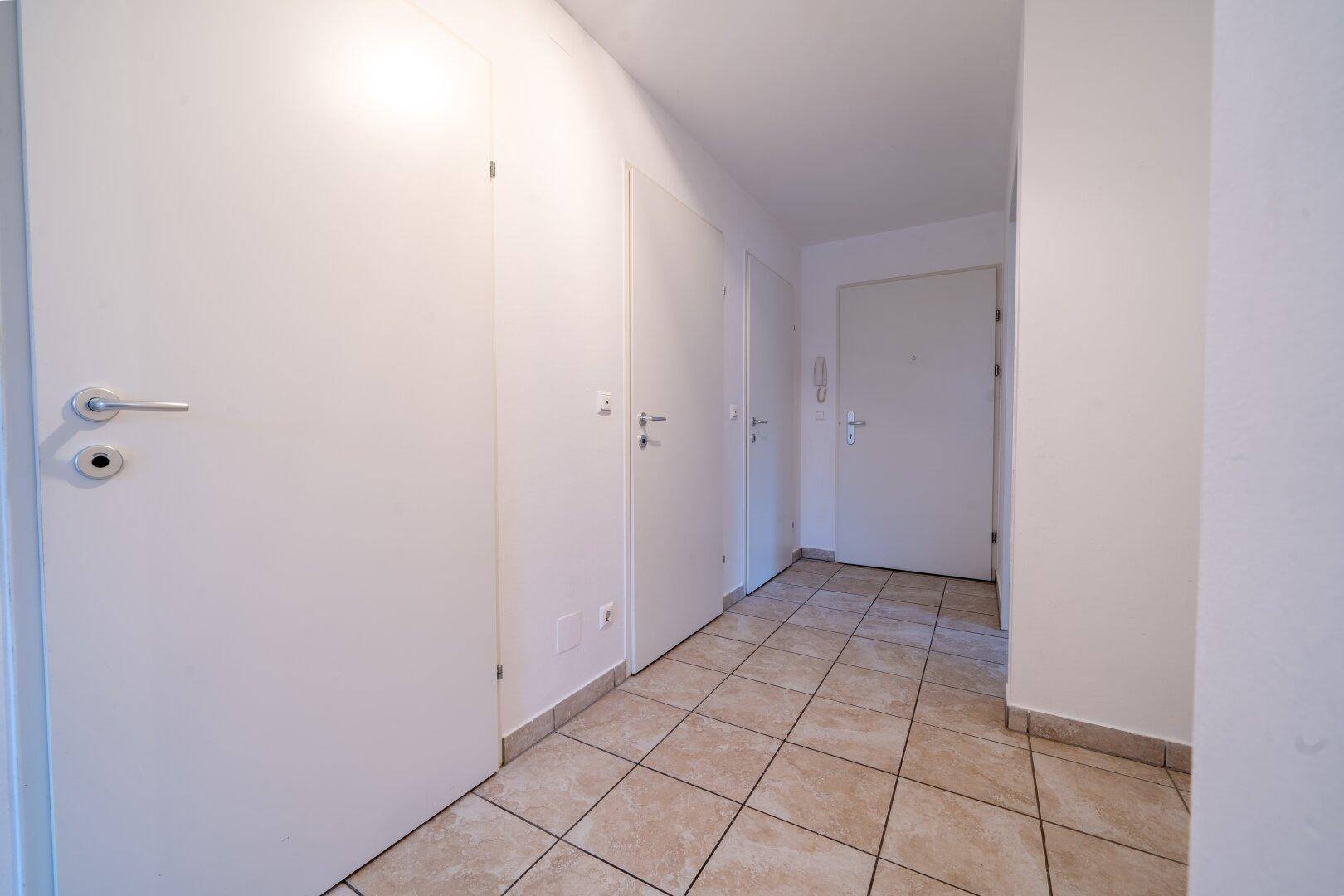 Geräumiger Flur mit beigefarbenen Fliesen und mehreren Türen, verbindet die Wohnbereiche.