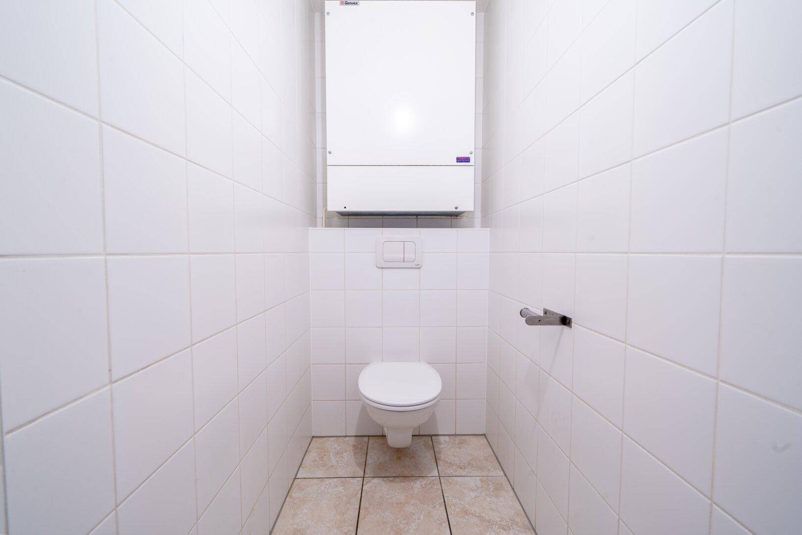 Modern gefliestes Gäste-WC mit wandhängender Toilette und weißer Wandverkleidung.