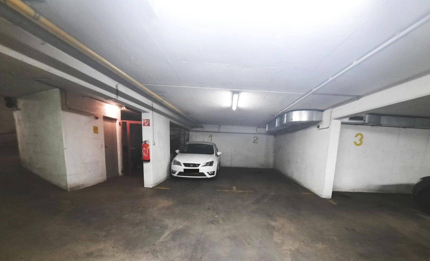 Helle Tiefgarage mit einem geparkten Auto und einem Feuerlöscher an der Wand, sauber und ordentlich.