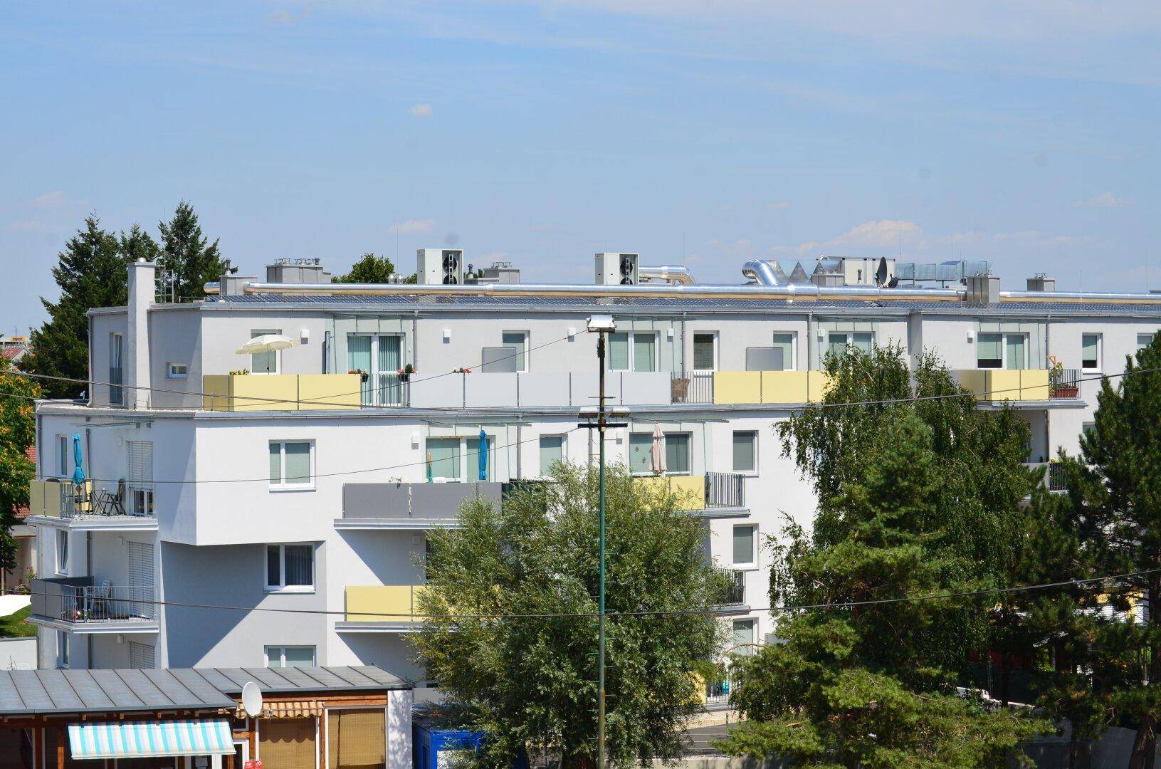 Mehrstöckiges Wohngebäude mit zahlreichen Balkonen und Dachterrassen, umgeben von Bäumen.