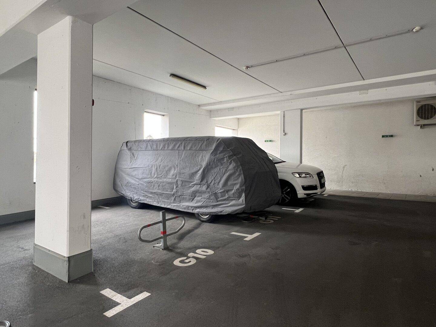 Tiefgarage mit einem abgedeckten Fahrzeug und einem Klimagerät an der Wand, gut beleuchtet.