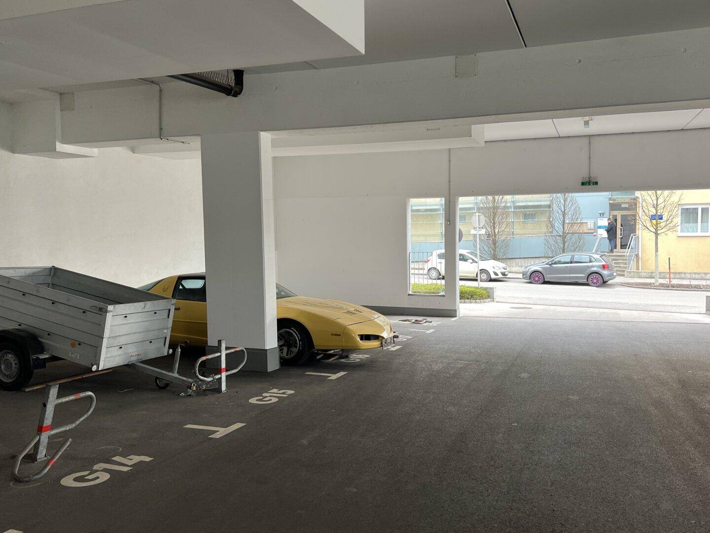Helle Tiefgarage mit einem gelben Sportwagen und einem Anhänger, mit Blick auf den Ausgangsbereich.