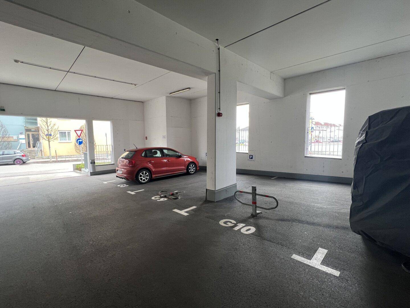Geräumige Tiefgarage mit einem roten Kleinwagen und markierten Stellplätzen, durch Fenster natürlich belichtet.