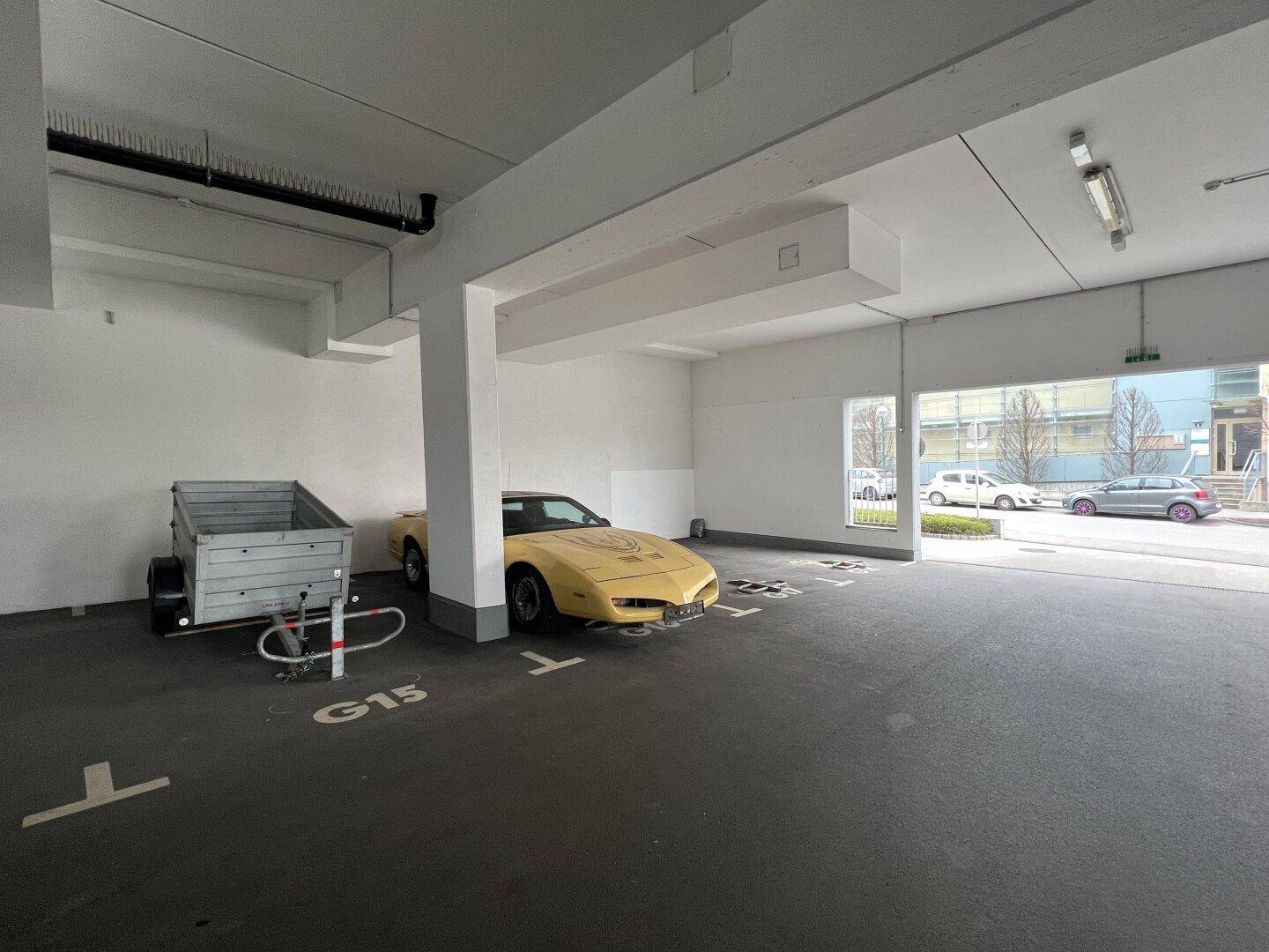 Tiefgarage mit einem gelben Sportwagen und einem Anhänger, gut beleuchtet und mit Blick nach draußen.
