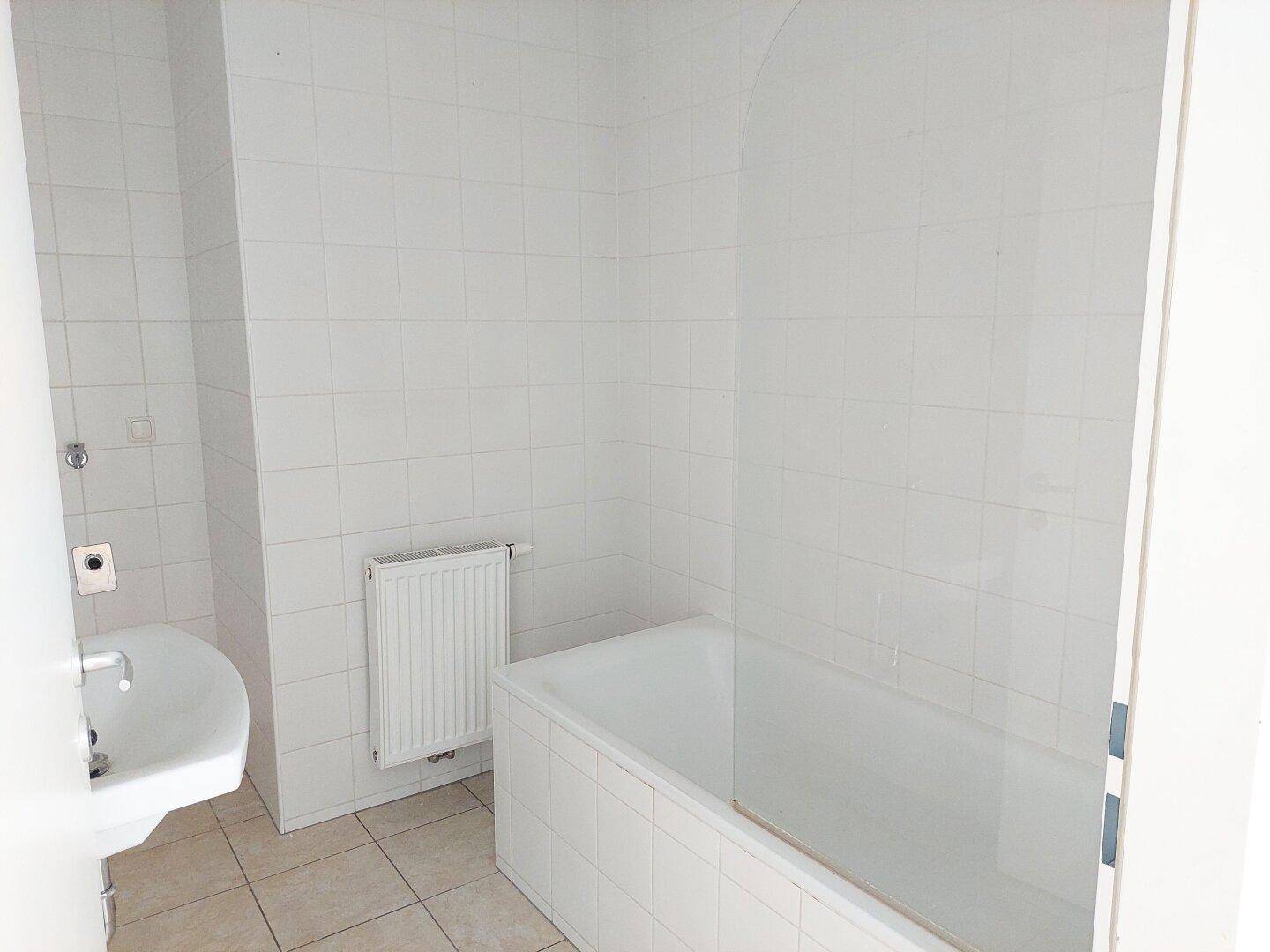 Badezimmer mit weißen Fliesen, Badewanne und Waschbecken.