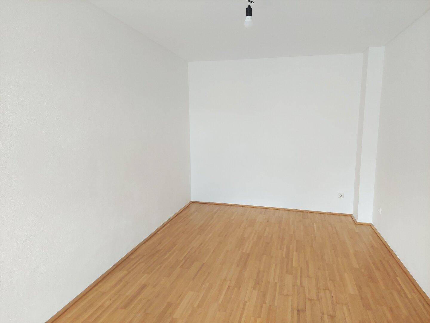 Schlichter Raum mit Parkettboden und weißen Wänden, ideal für ein Schlafzimmer.