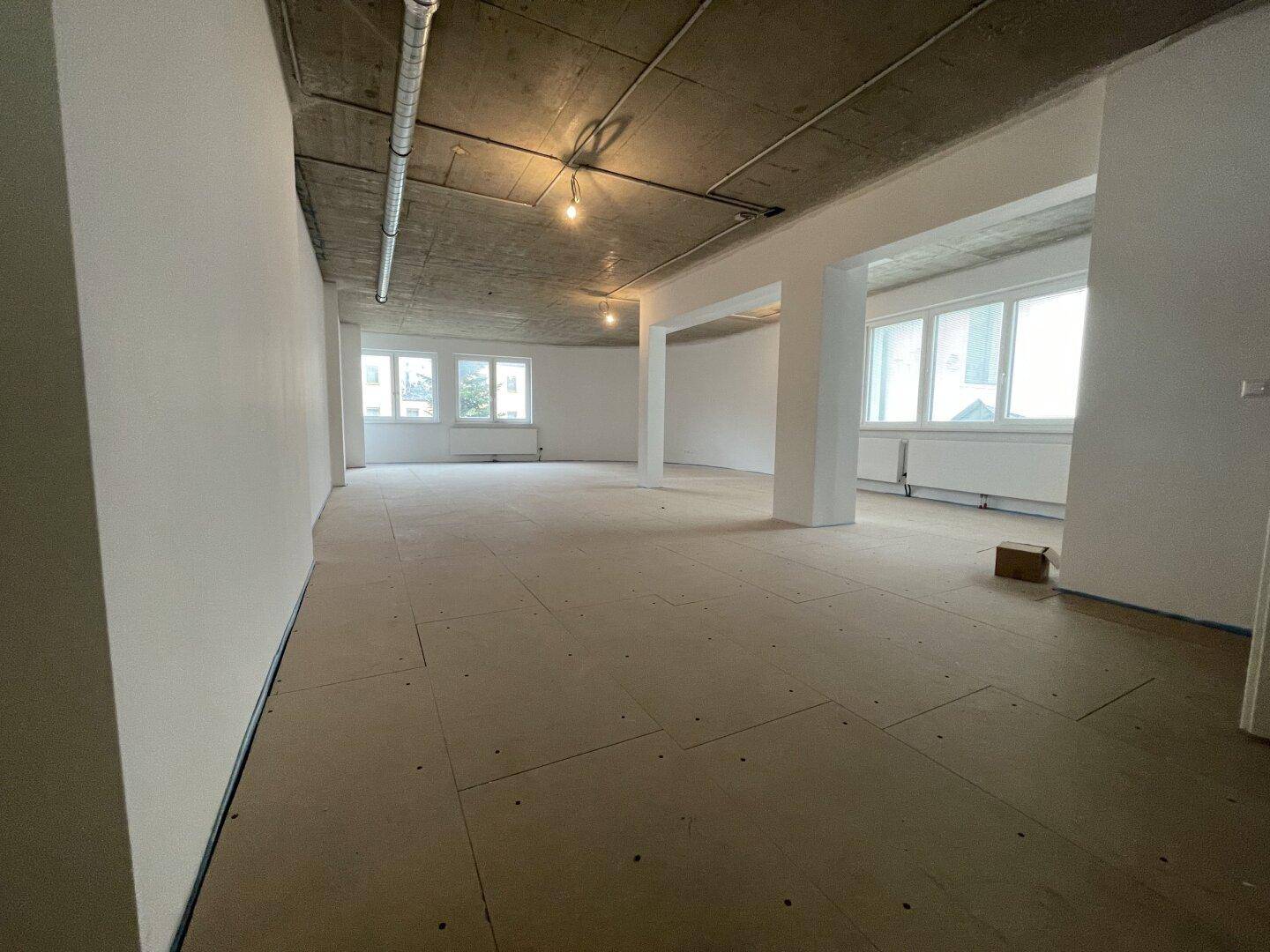 Weitläufiger Gewerberaum im Rohbau mit hohen Decken und großen Fenstern, ideal für individuelle Gestaltung.